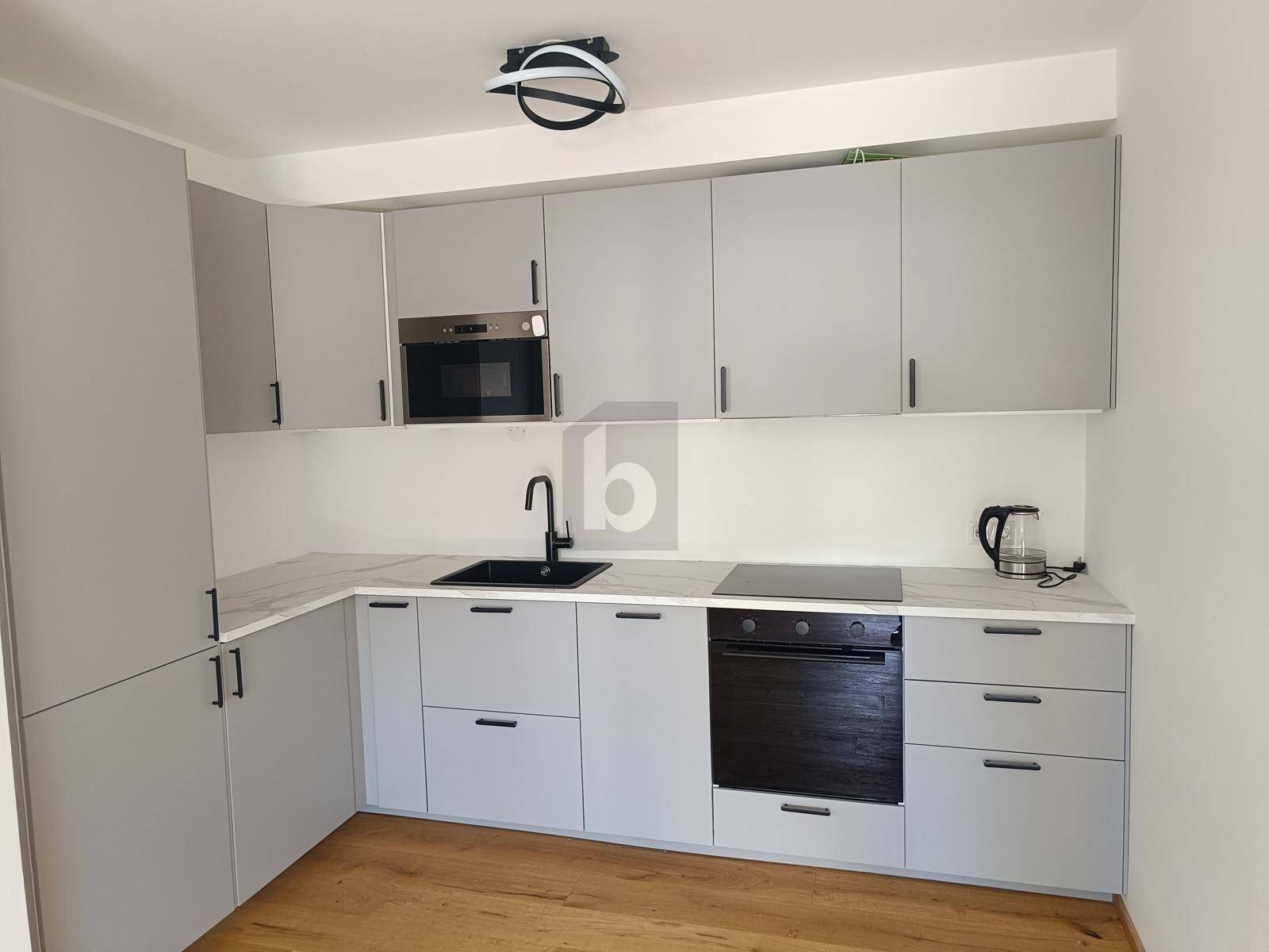 Moderne Küche mit grauen Schränken, weißer Arbeitsplatte und integrierten Geräten auf Holzboden.