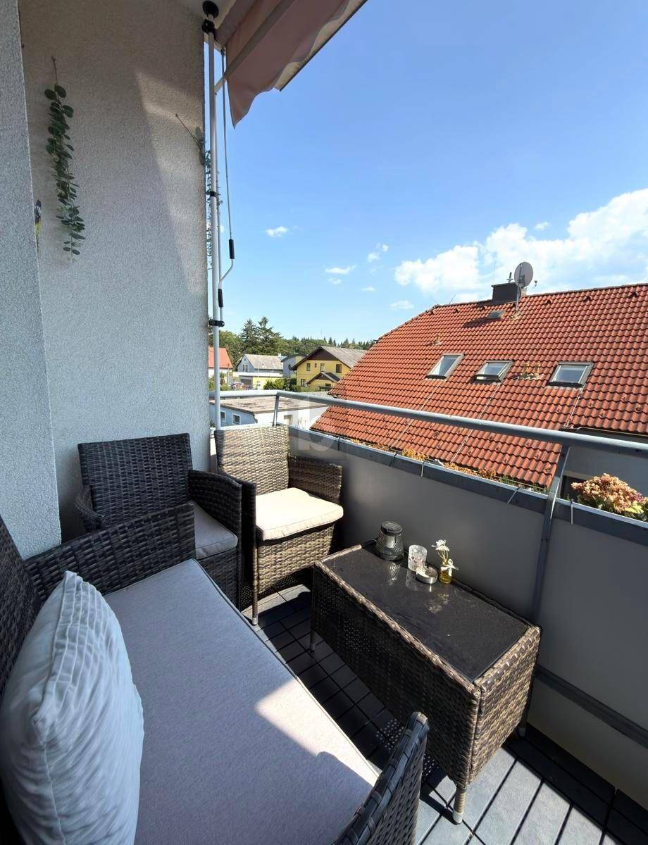 Möblierter Balkon mit Rattan-Sitzgruppe und Blick auf die umliegenden Dächer und den Himmel.