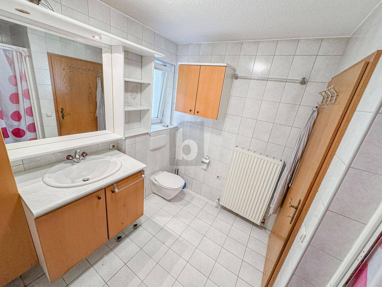 Badezimmer mit weißen Fliesen, Waschbecken, Toilette und Duschvorhang.