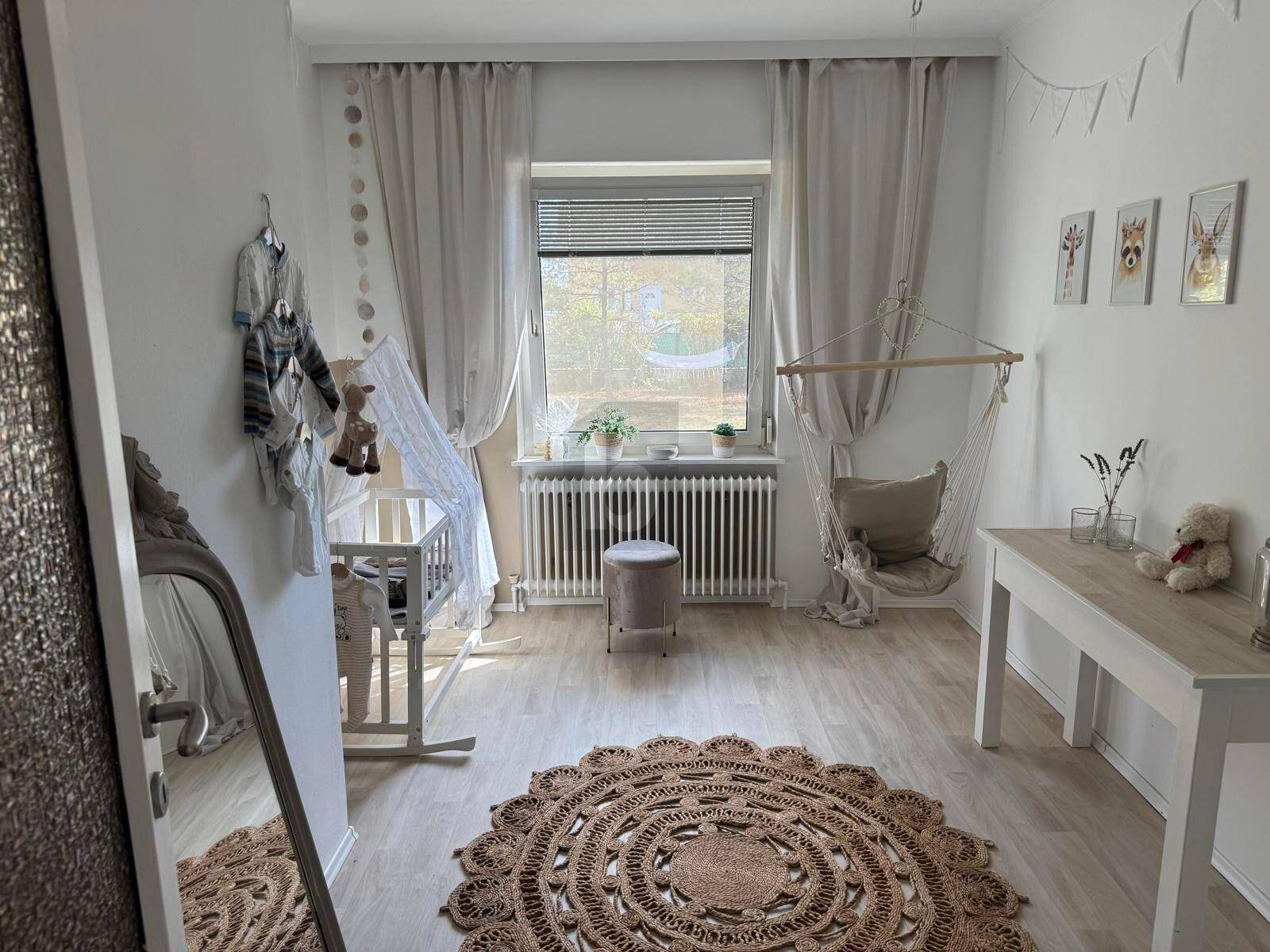 Helles Kinderzimmer mit Babybett, Schaukelstuhl und Laminatboden, ideal für ein Kleinkind.