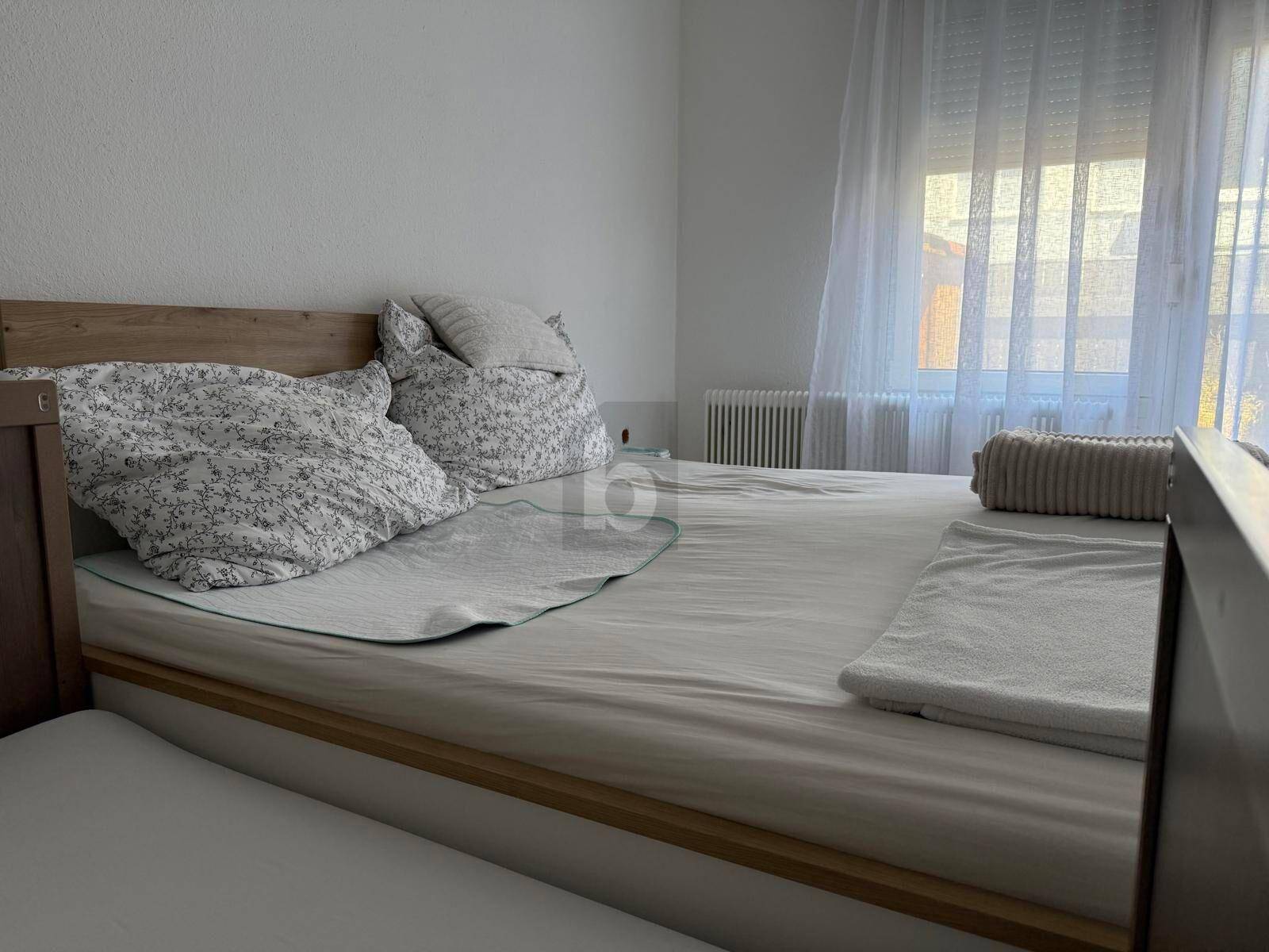 Helles Schlafzimmer mit einem Holzbett und einem Fenster mit transparenten Vorhängen.