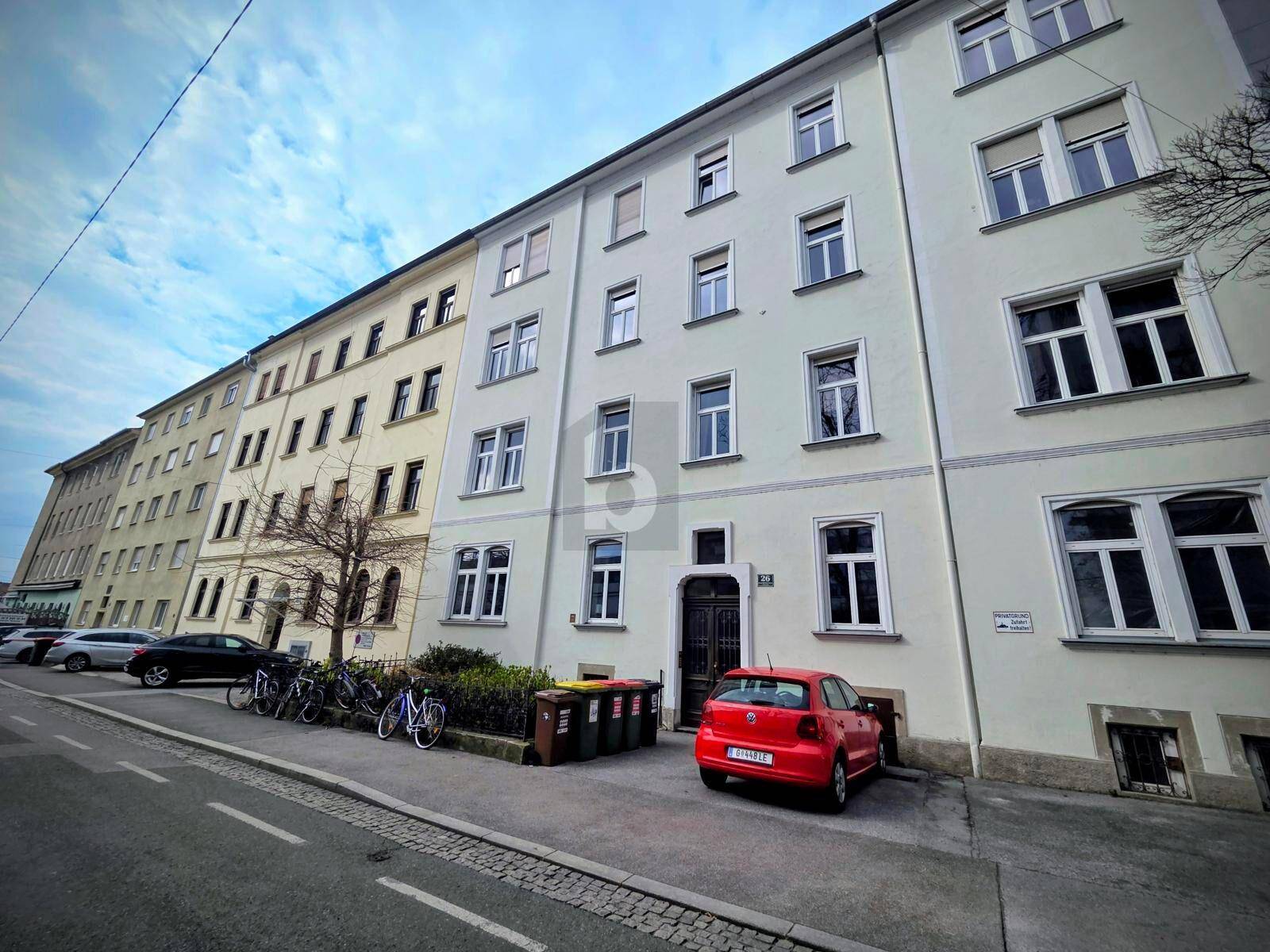 Mehrfamilienhaus mit klassischer Fassade an einer städtischen Straße mit parkenden Fahrzeugen.