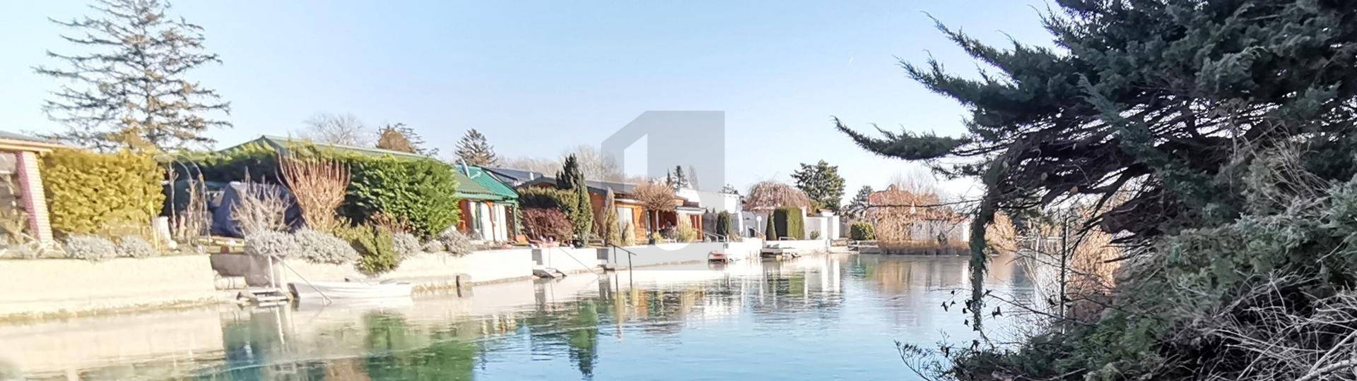 Weitläufiger Blick auf einen Kanal mit Häusern und Bäumen entlang der Uferlinie unter klarem Himmel.