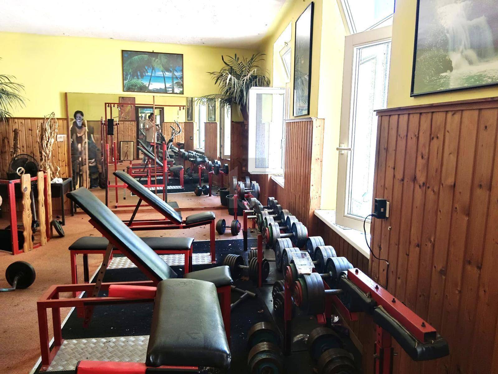 Fitnessraum mit verschiedenen Hanteln, Trainingsbänken und Holzvertäfelung an den Wänden.