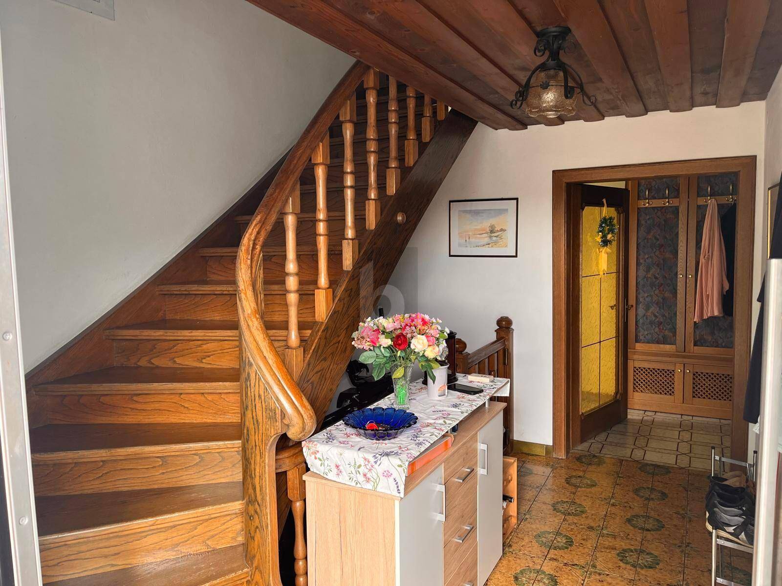 Eingangsbereich mit geschwungener Holztreppe, Holzbalkendecke und Fliesenboden.
