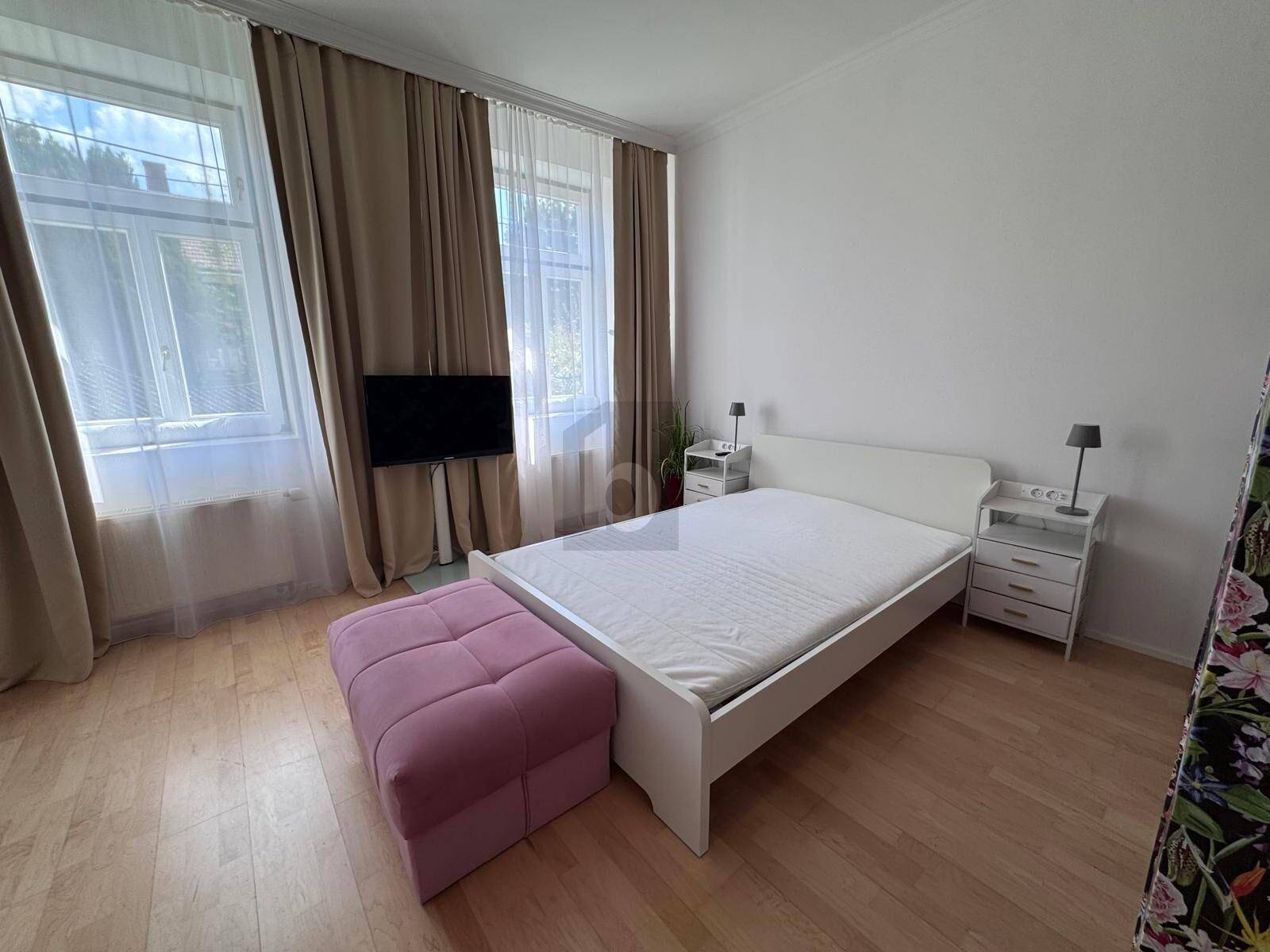 Helles Schlafzimmer mit Parkettboden, großem Fenster und einem Doppelbett mit Nachttischen.