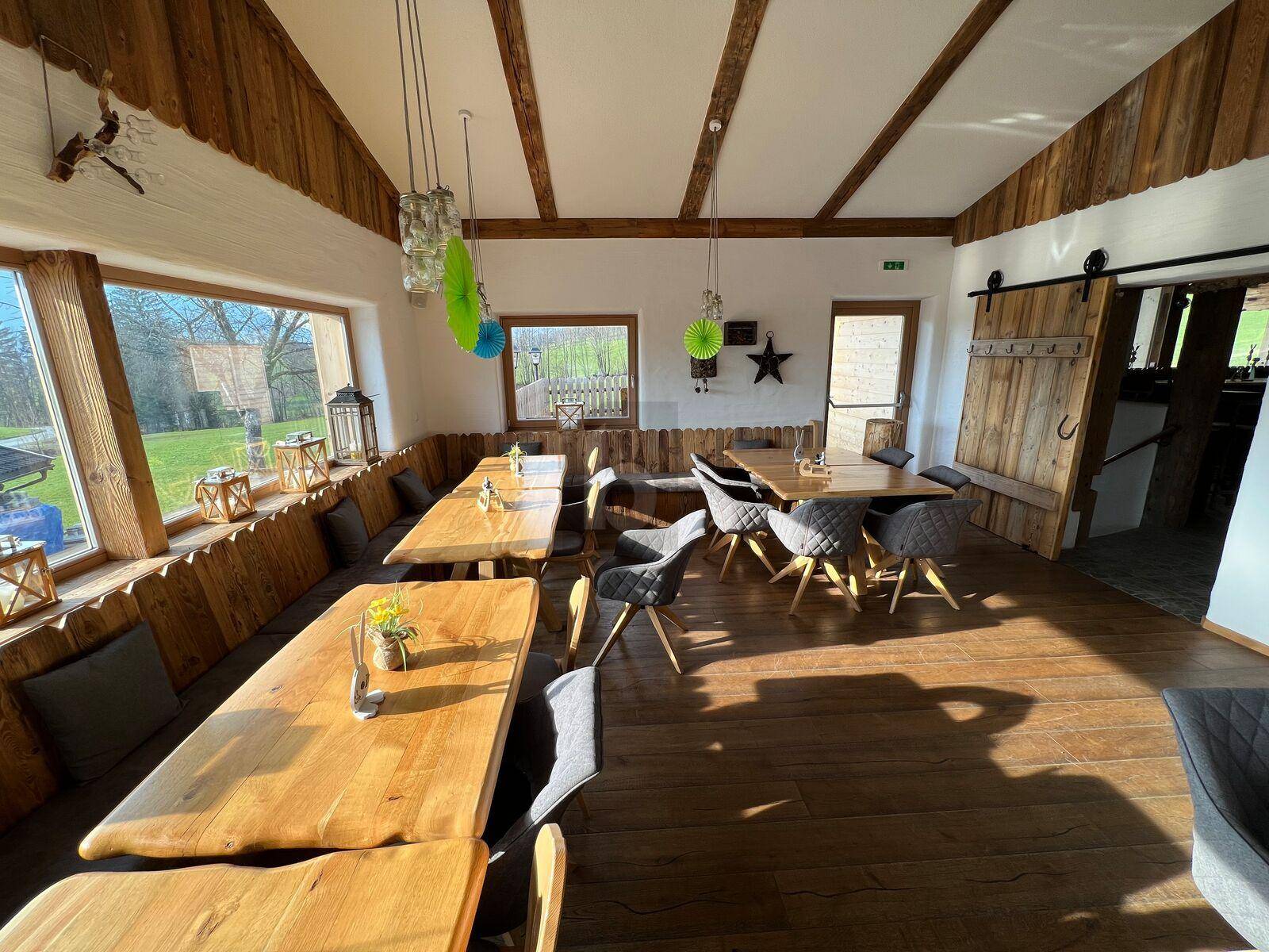 Heller Essbereich mit Holzböden und rustikalen Holztischen, umgeben von großen Fenstern mit Ausblick.
