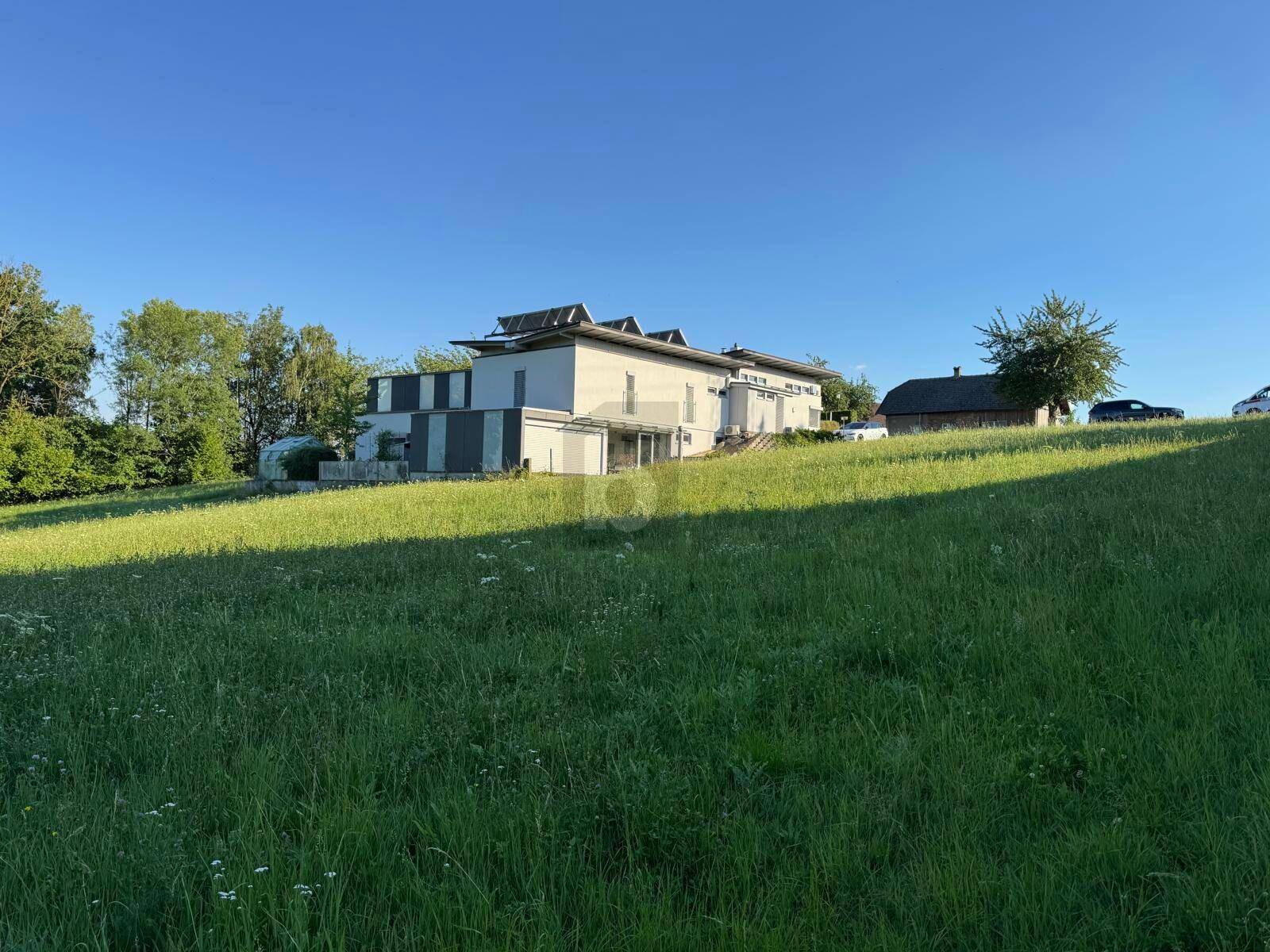 Modernes Haus mit Photovoltaikanlage auf einem grünen Hügel, umgeben von Natur.