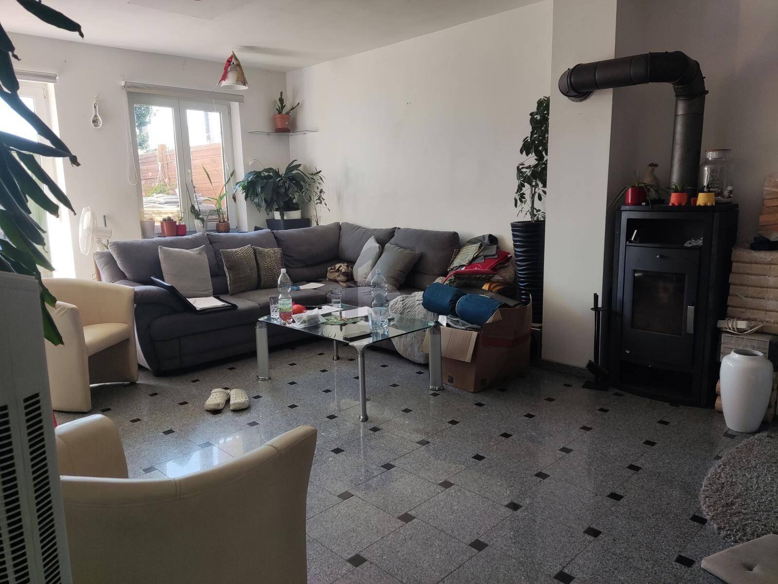 Geräumiges Wohnzimmer mit einem Kaminofen, Fliesenboden und einer großen Eckcouch.