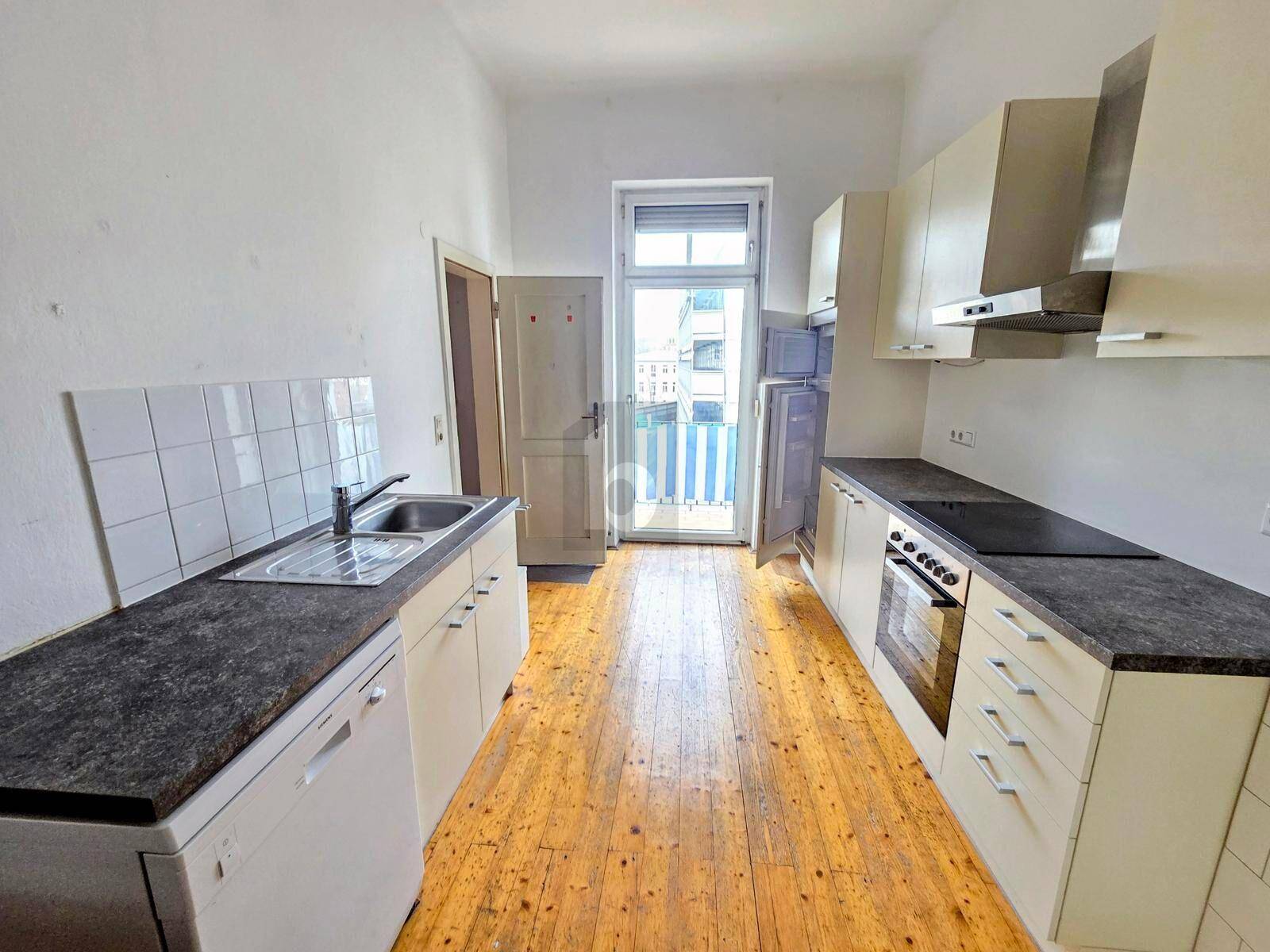Funktionale Küche mit weißen Schränken, dunklen Arbeitsplatten und Zugang zu einem kleinen Balkon.