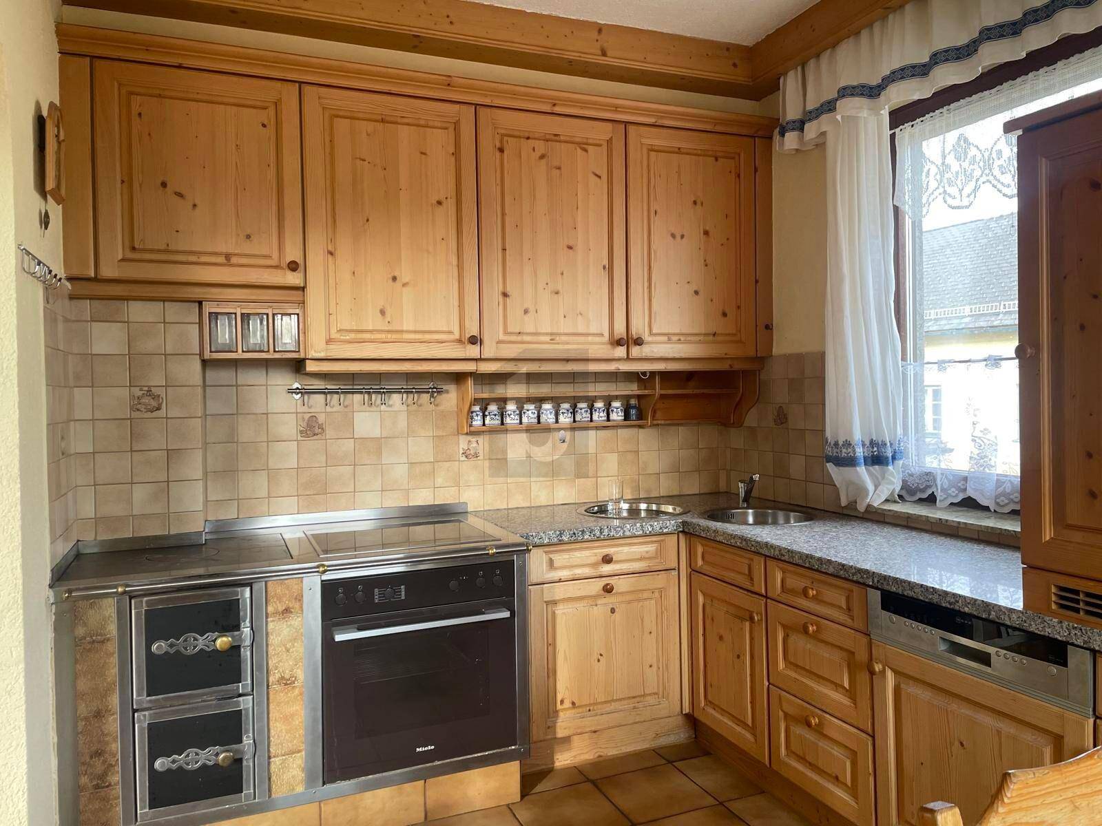Traditionelle Holzküche mit integrierten Geräten, Granitarbeitsplatte und Fenster mit Vorhängen.