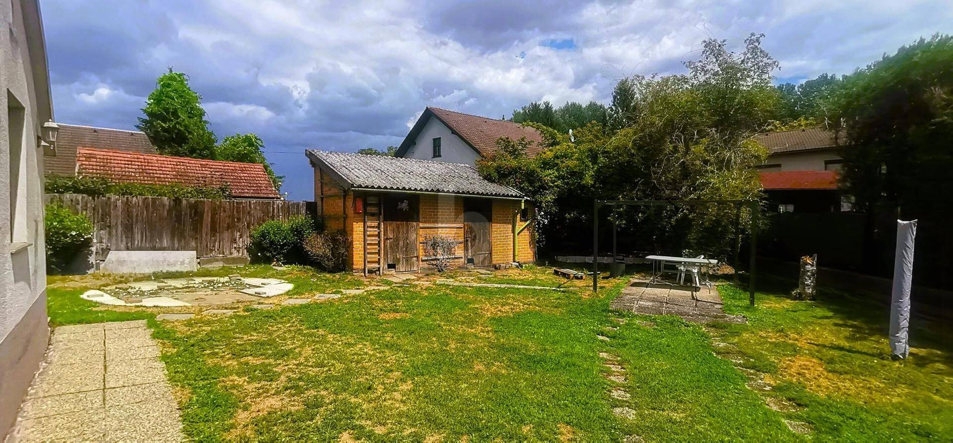 Großer Garten mit Rasenfläche, Gartenhaus und einem Tisch im Freien.