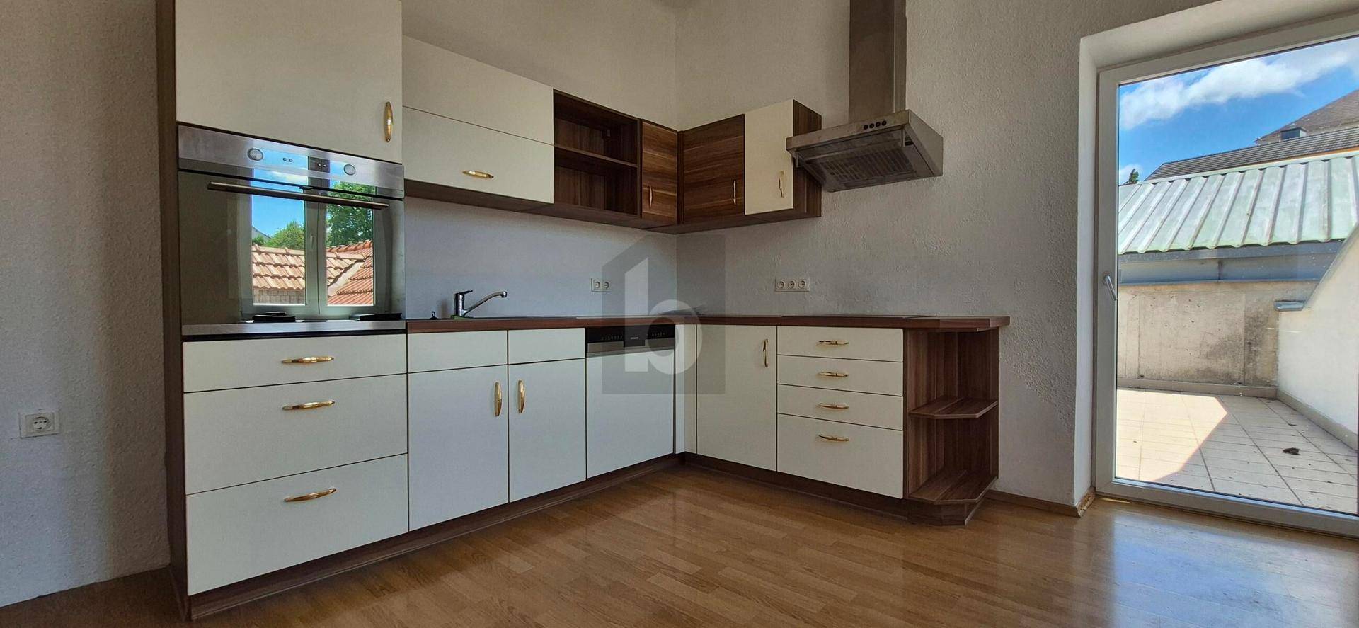 Moderne Küche mit weißen und holzfarbenen Schränken und Zugang zu einer Terrasse.