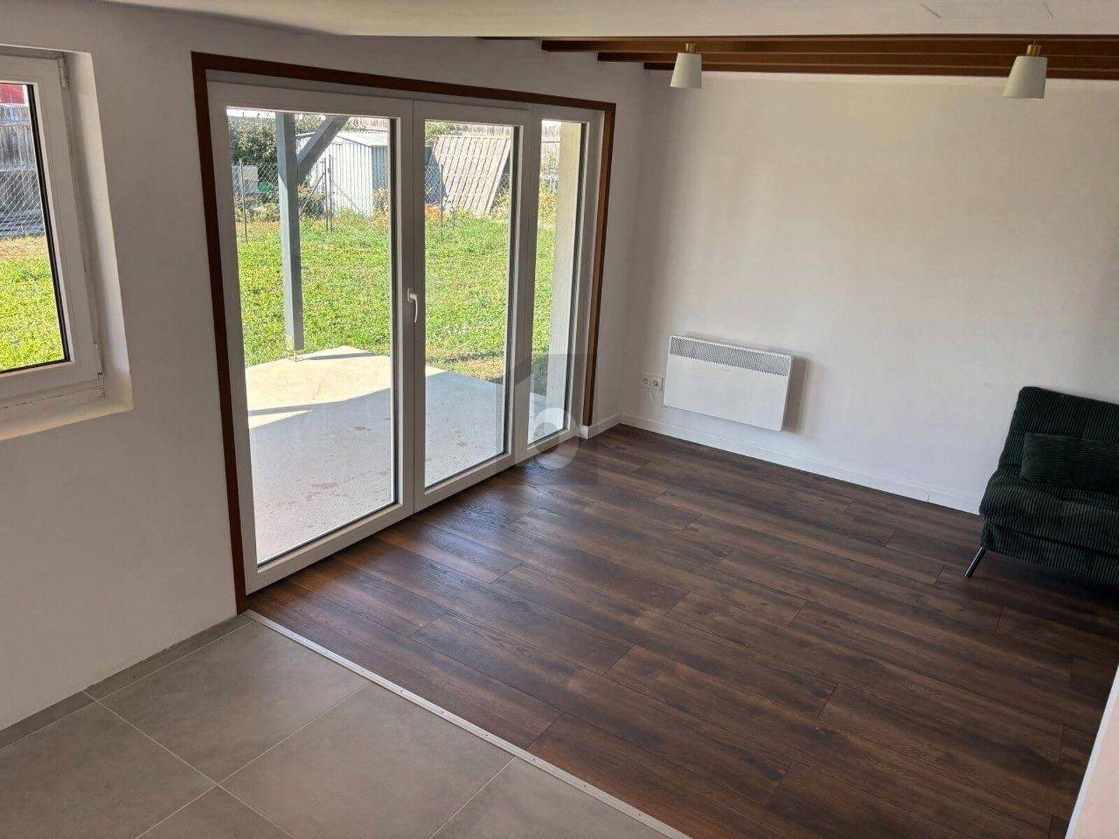 Heller Wohnraum mit dunklem Holzboden, großen Terrassentüren und Blick ins Grüne.