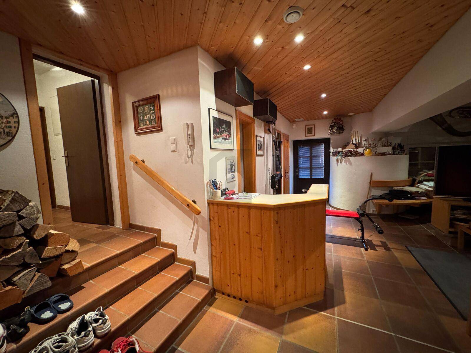 Rustikaler Eingangsbereich mit Holzdecke, Fliesenboden und Holztreppe.