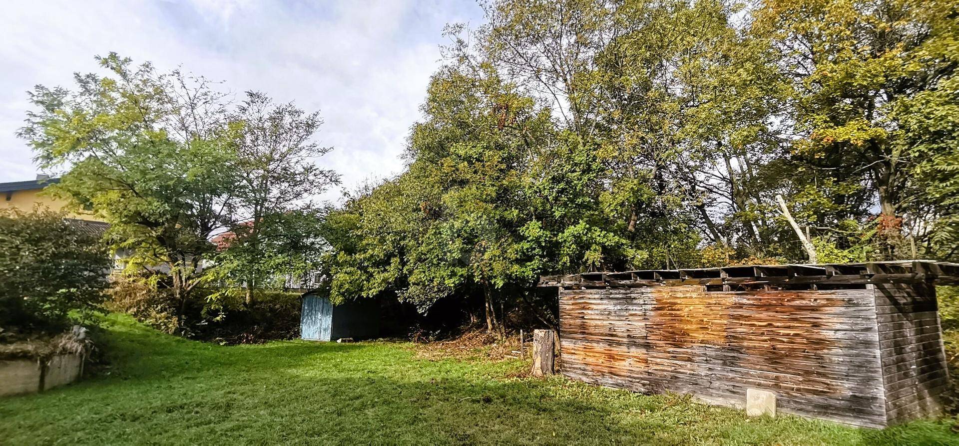 Weitläufiger Garten mit Rasenfläche, zwei Holzschuppen und altem Baumbestand.