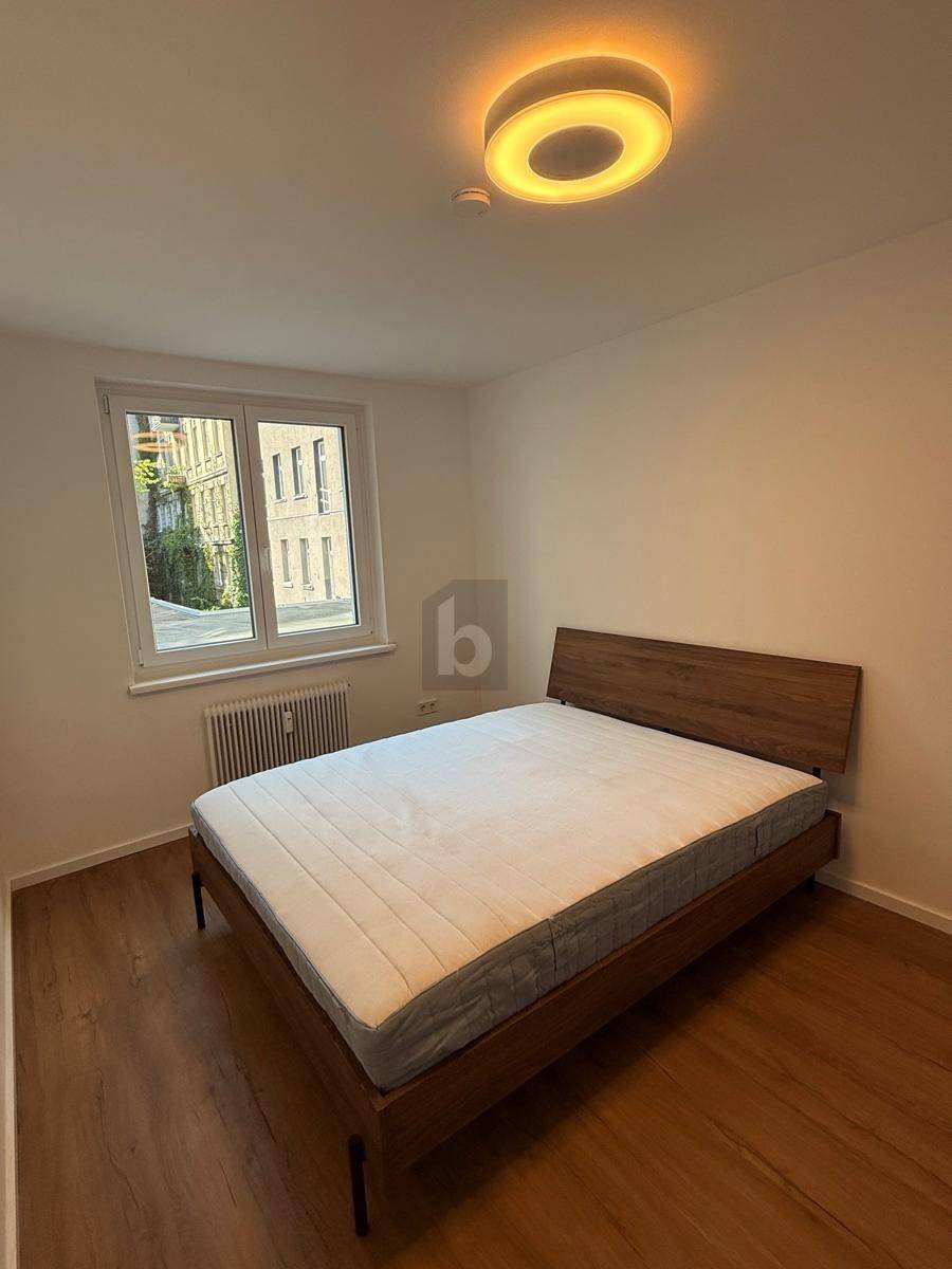 Schlafzimmer mit Holzbettrahmen, Holzboden und einem Fenster, das den Raum erhellt.
