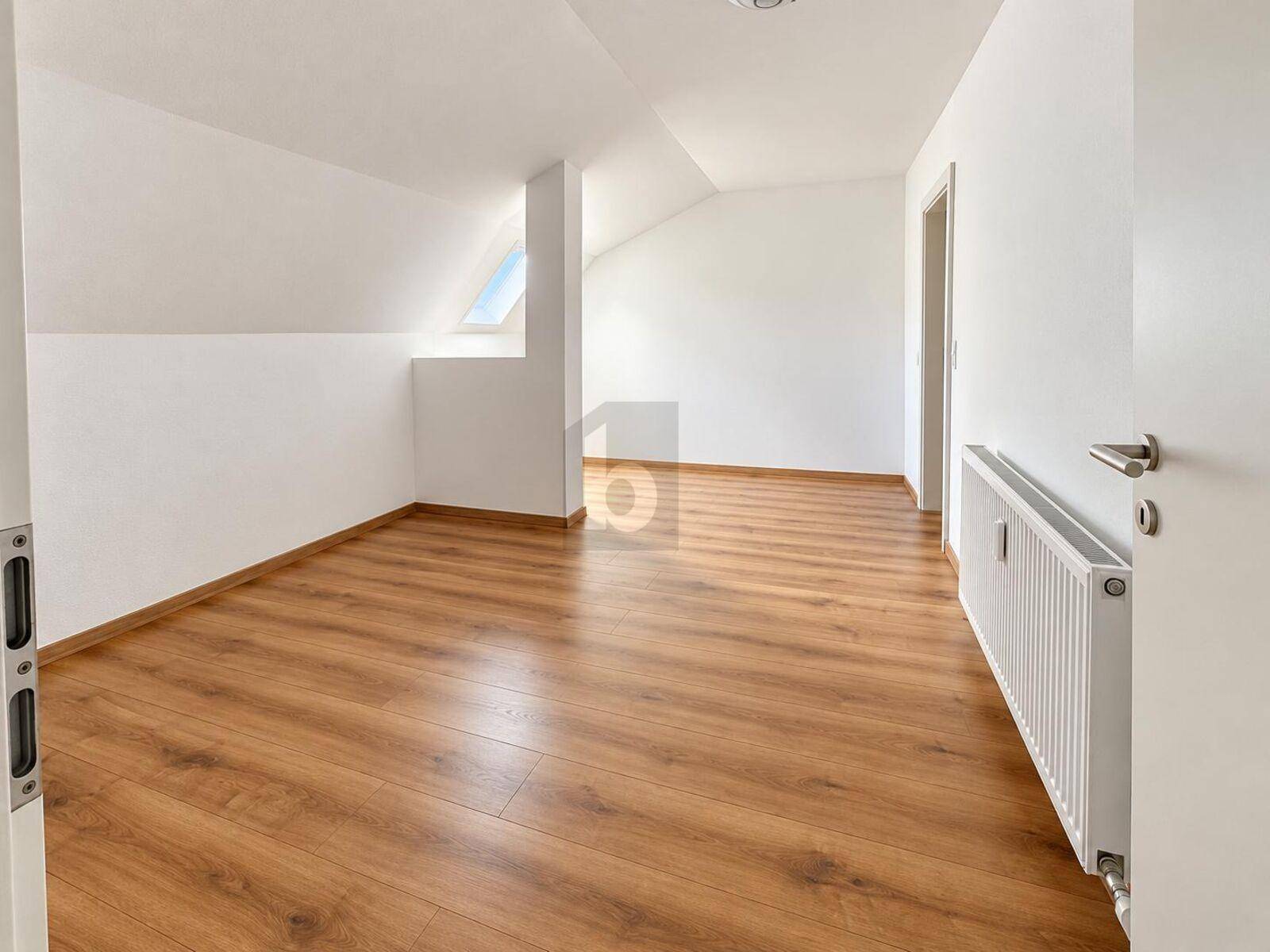 Freundliches Zimmer mit Laminatboden, Dachschräge und Dachfenster für viel Tageslicht.