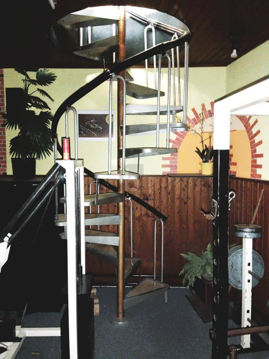 Wendeltreppe in einem Fitnessraum mit Holzvertäfelung und gelben Wänden.