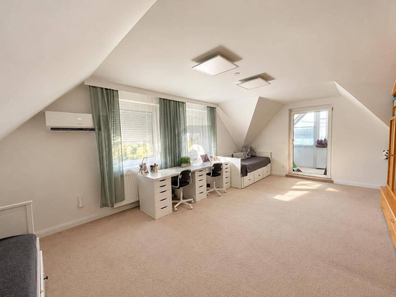 Geräumiges Dachzimmer mit Schrägen, zwei Schreibtischen und Zugang zu einem kleinen Balkon.