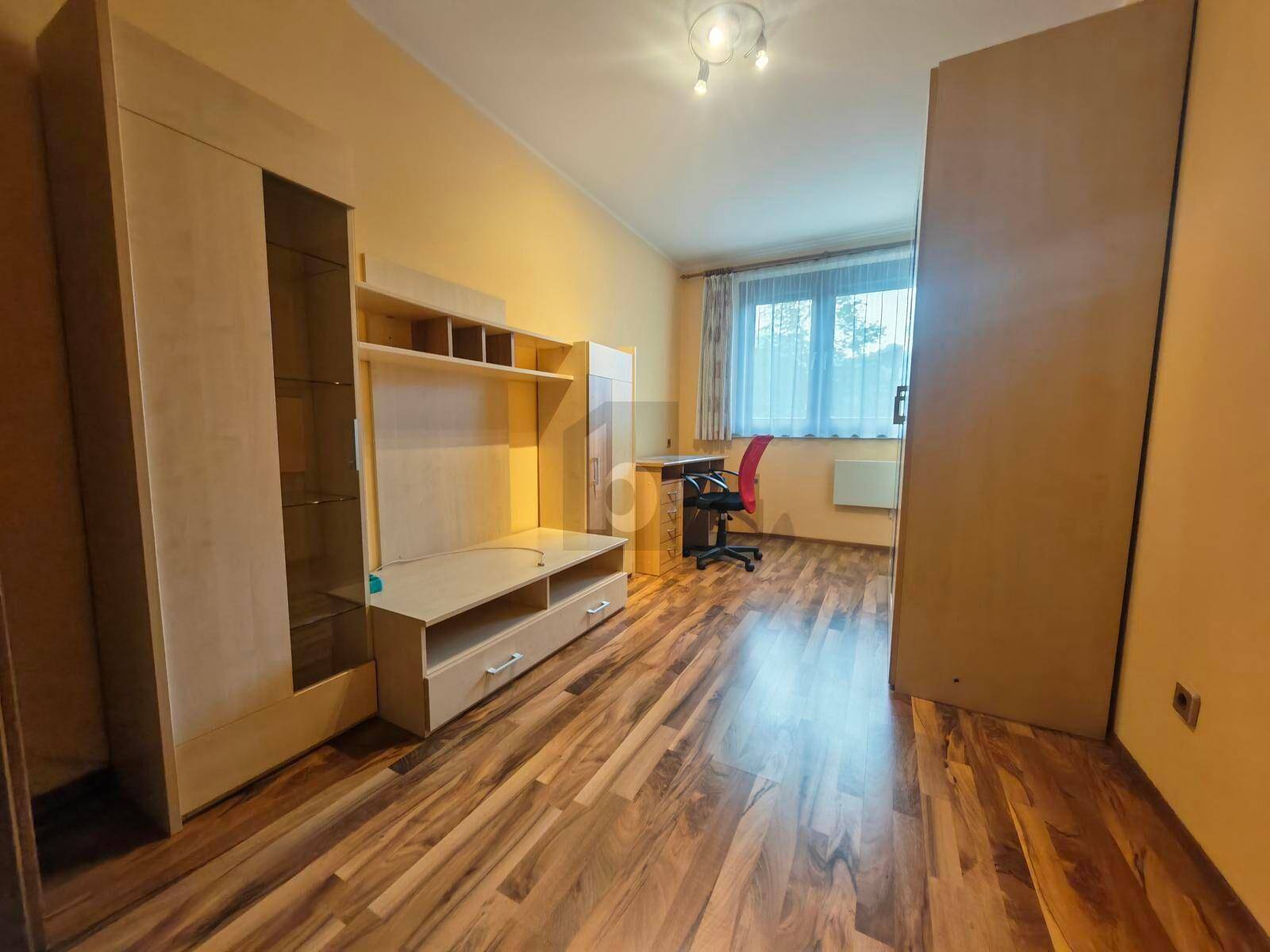Helles Zimmer mit Laminatboden, Holzschränken und einem Arbeitsbereich unter dem Fenster.