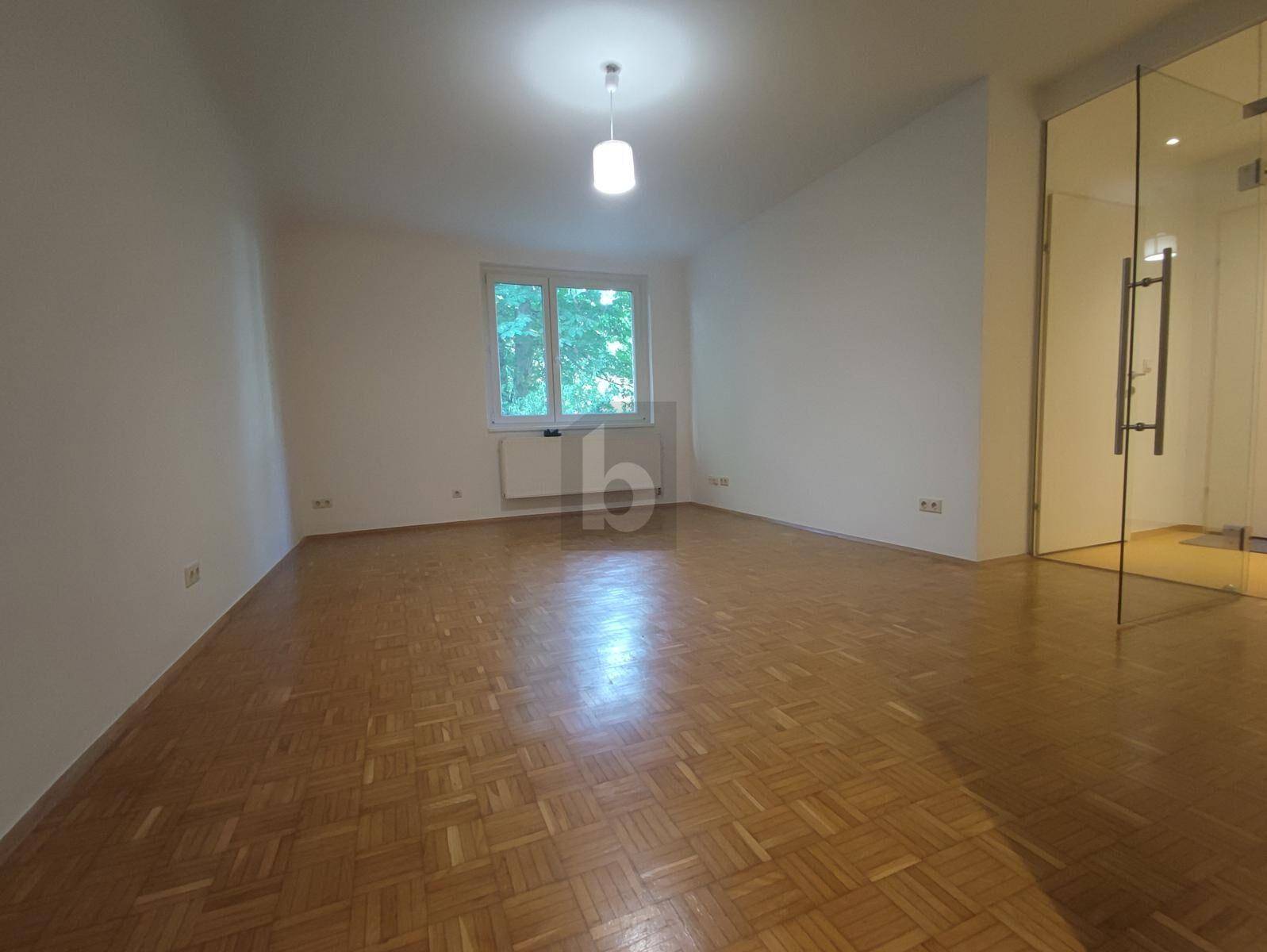 Geräumiges Wohnzimmer mit Fischgrätparkett, großen Fenstern und Blick ins Grüne.