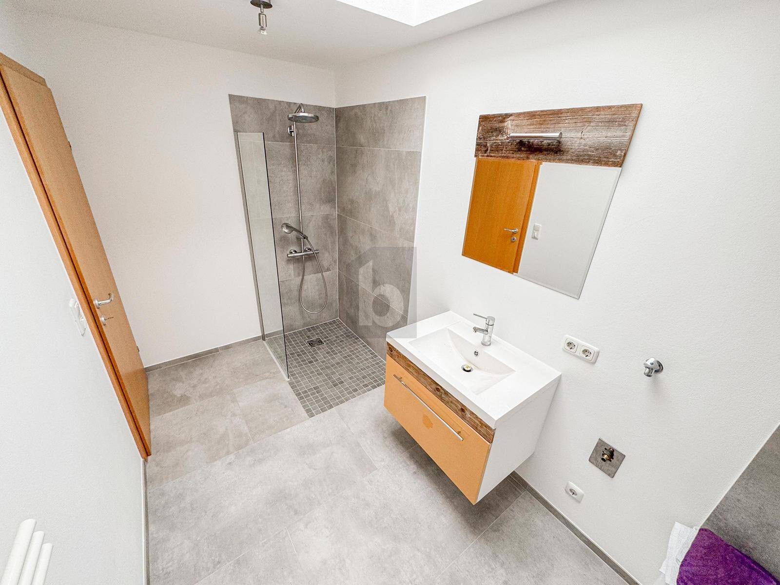 Modernes Badezimmer mit begehbarer Dusche, großformatigen Fliesen und einem Waschbecken mit Holzunterschrank.