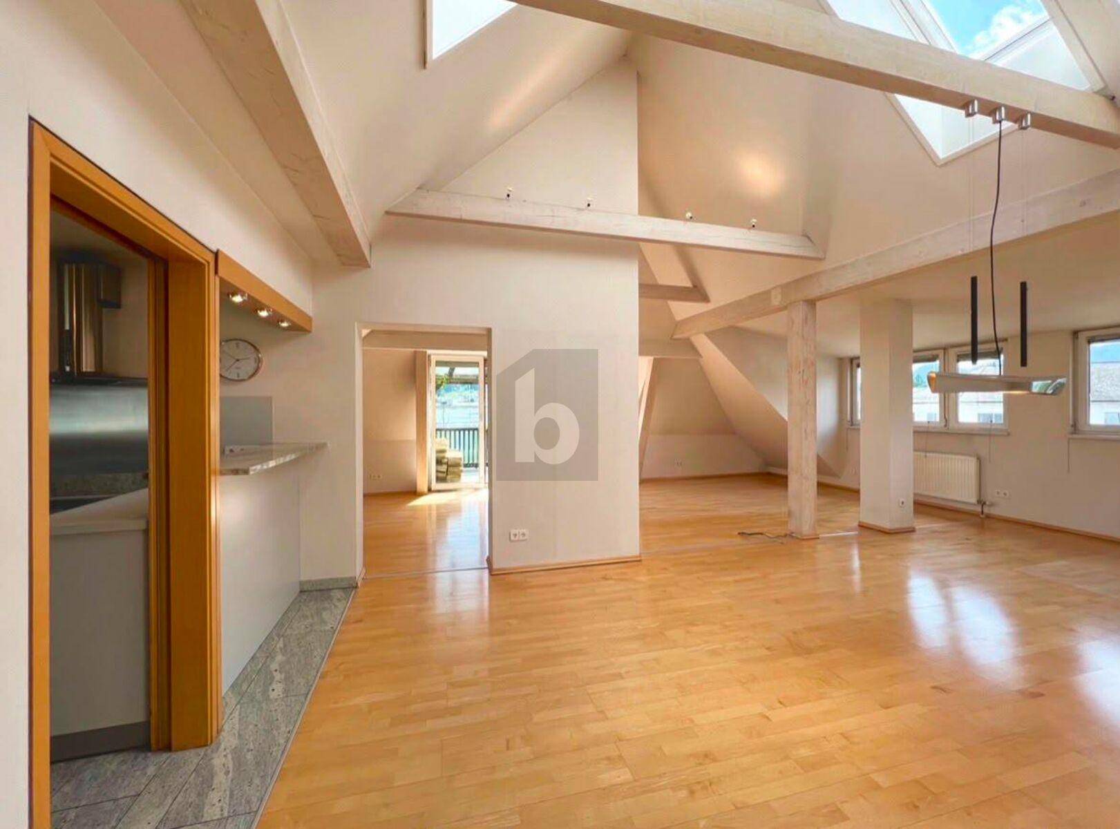 Heller Wohnbereich im Dachgeschoss mit sichtbaren Holzbalken, Dachfenstern und Parkettboden.