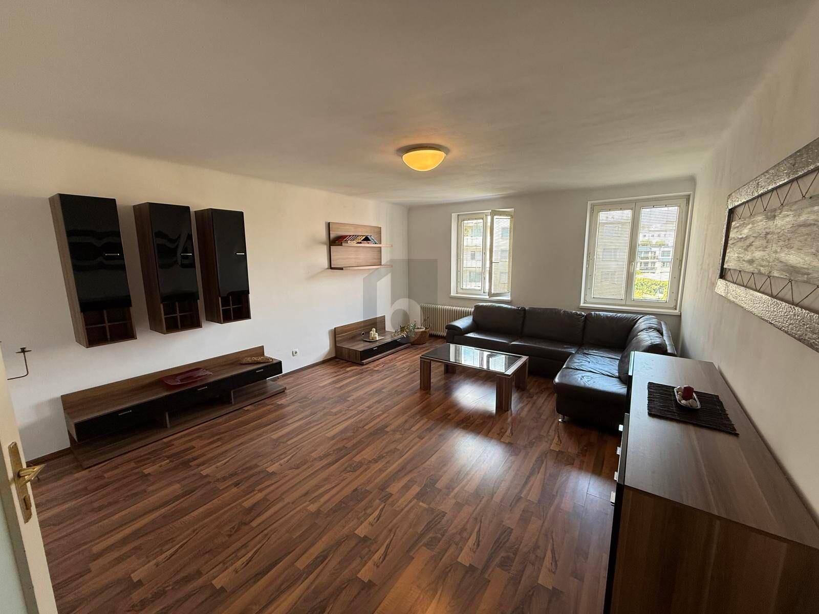 Geräumiges Wohnzimmer mit dunklem Ecksofa, modernen Möbeln und viel Tageslicht.