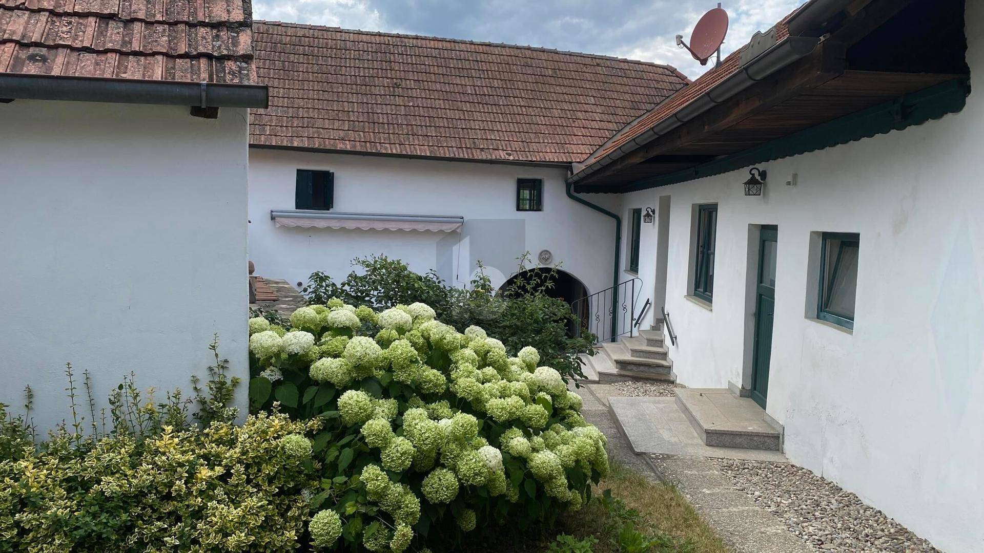 Innenhof mit weiß getünchten Gebäuden, üppigem Grün und traditionellen Dachziegeln.