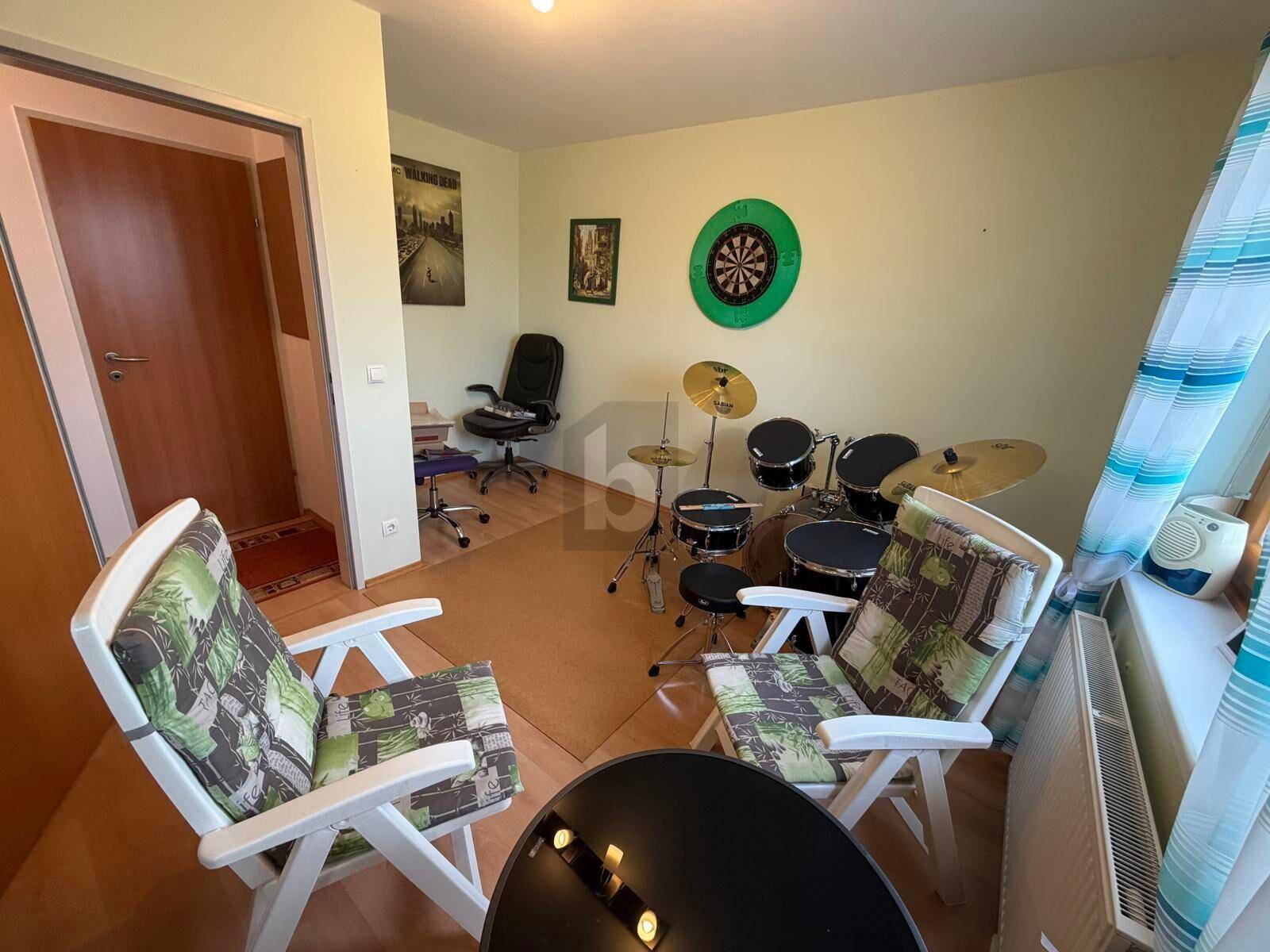 Vielseitiger Raum mit Schlagzeug, Dartscheibe und Sitzgelegenheiten, ideal für Hobbys.