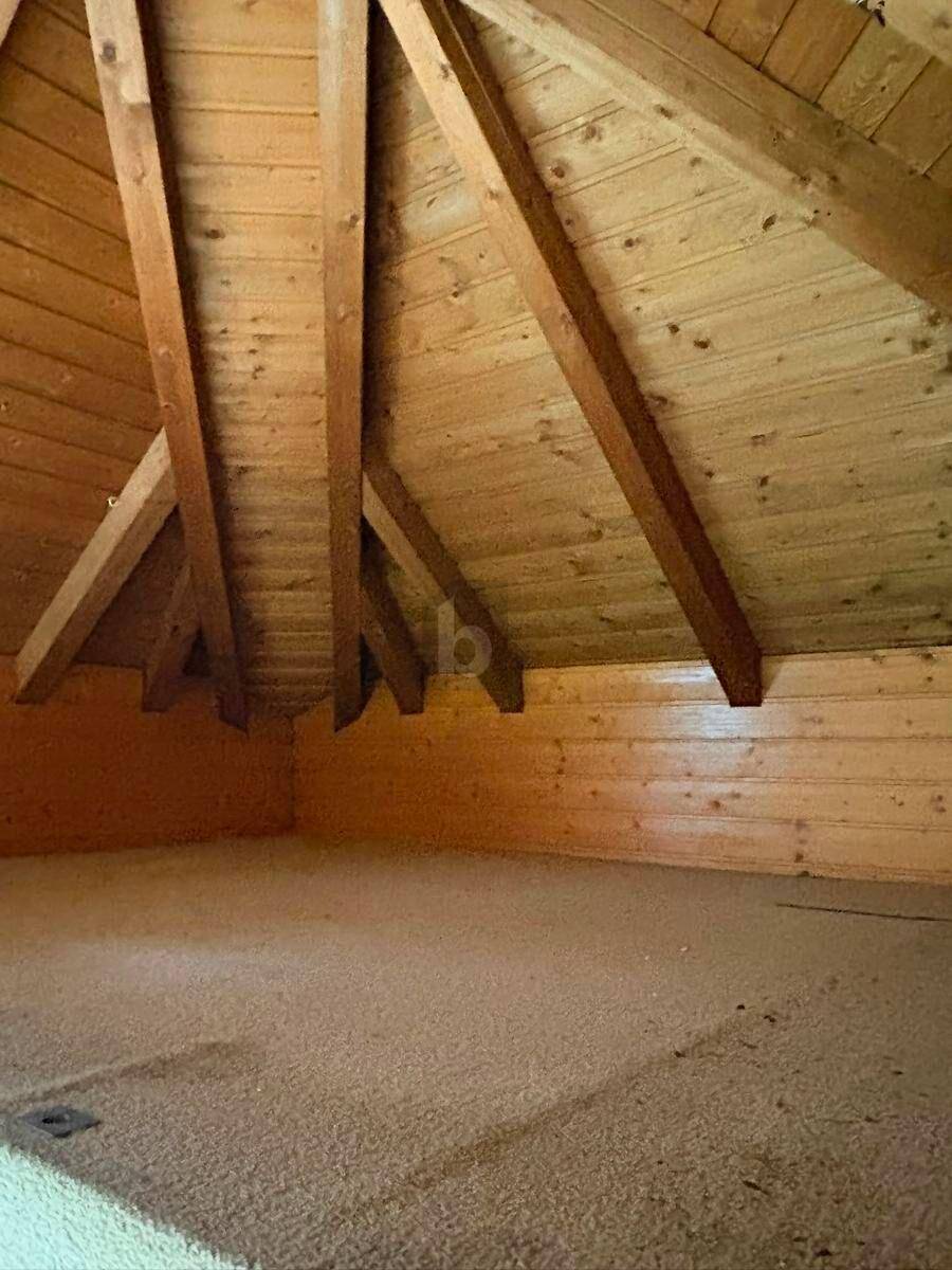 Gemütlicher Dachbodenraum mit sichtbaren Holzbalken und schrägen Wänden, komplett holzvertäfelt.