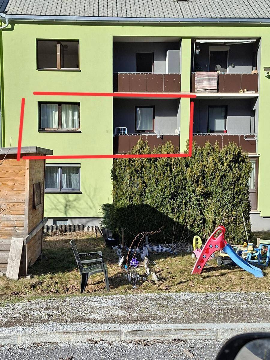 Außenansicht eines Mehrfamilienhauses mit Balkonen und kleinem Gartenbereich.