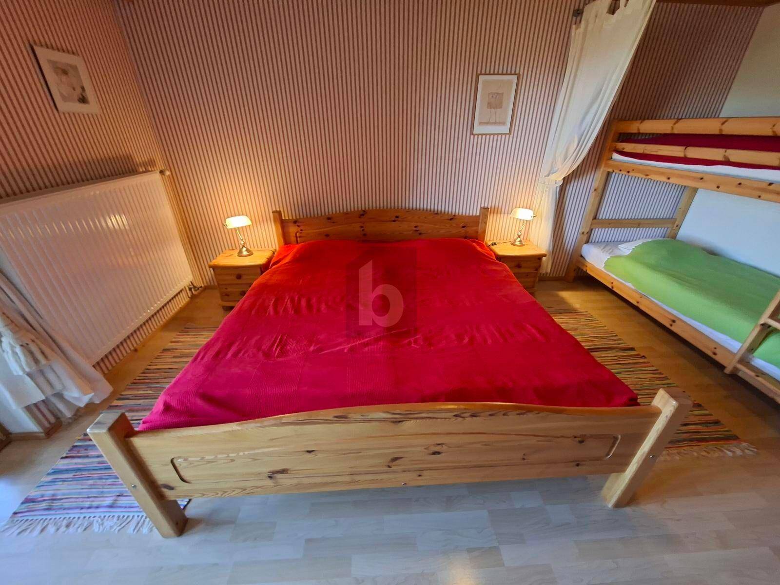 Gemütliches Schlafzimmer mit großem Holzbett, roter Bettwäsche und Etagenbett für Gäste.