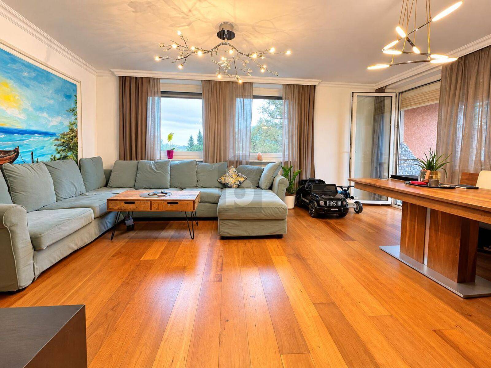 Geräumiger Wohn- und Essbereich mit Holzboden, großem Sofa und Zugang zum Balkon.