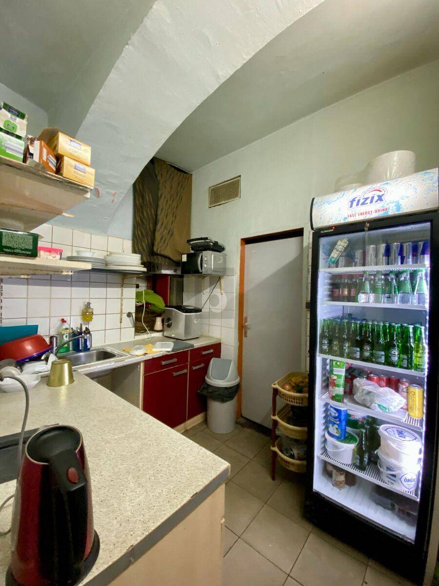 Funktionale Küche mit Edelstahlspüle, Regalen, Mikrowelle und einem großen Getränkekühlschrank.