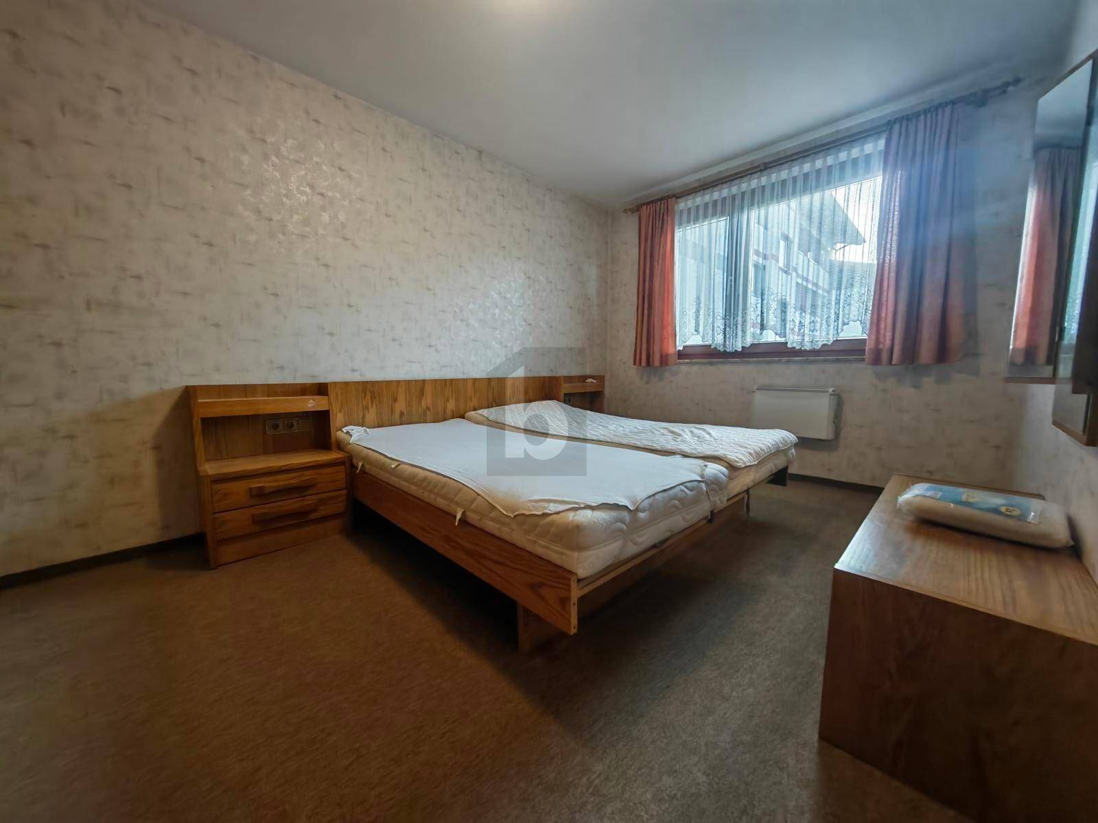 Schlafzimmer mit zwei Einzelbetten, Holzmöbeln und gemusterter Tapete, bietet eine einfache Einrichtung.