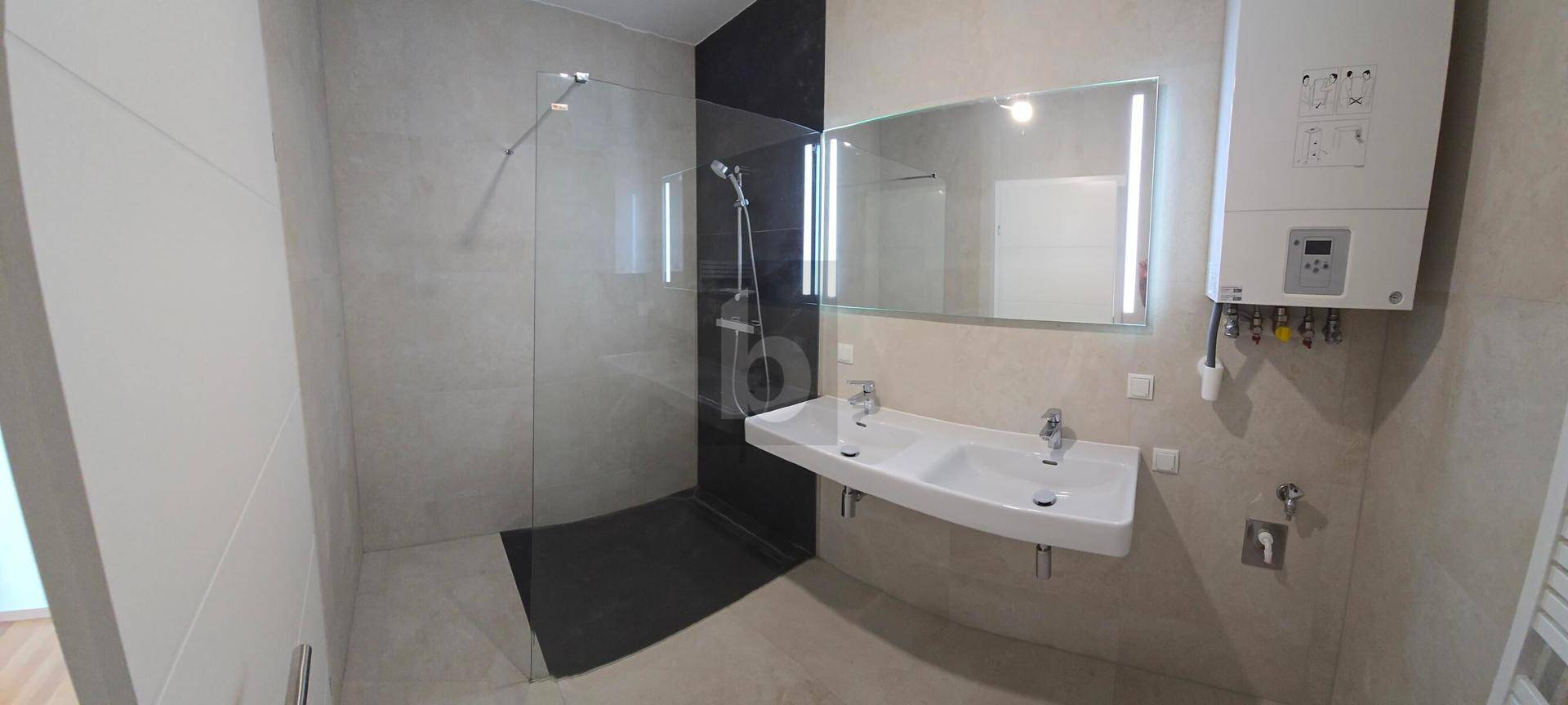 Modernes Badezimmer mit Doppelwaschbecken, großer begehbarer Dusche und beleuchtetem Spiegel.