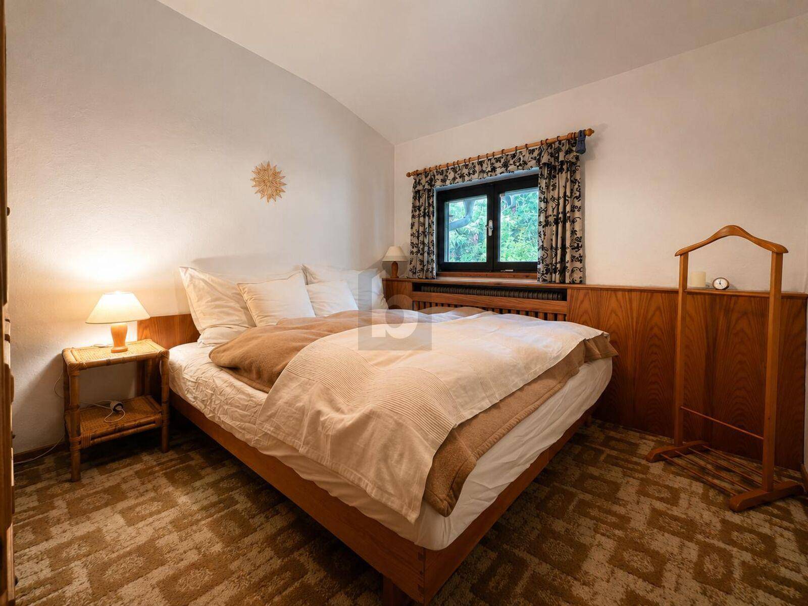 Gemütliches Schlafzimmer mit Holztäfelung, Teppichboden und Blick ins Grüne.