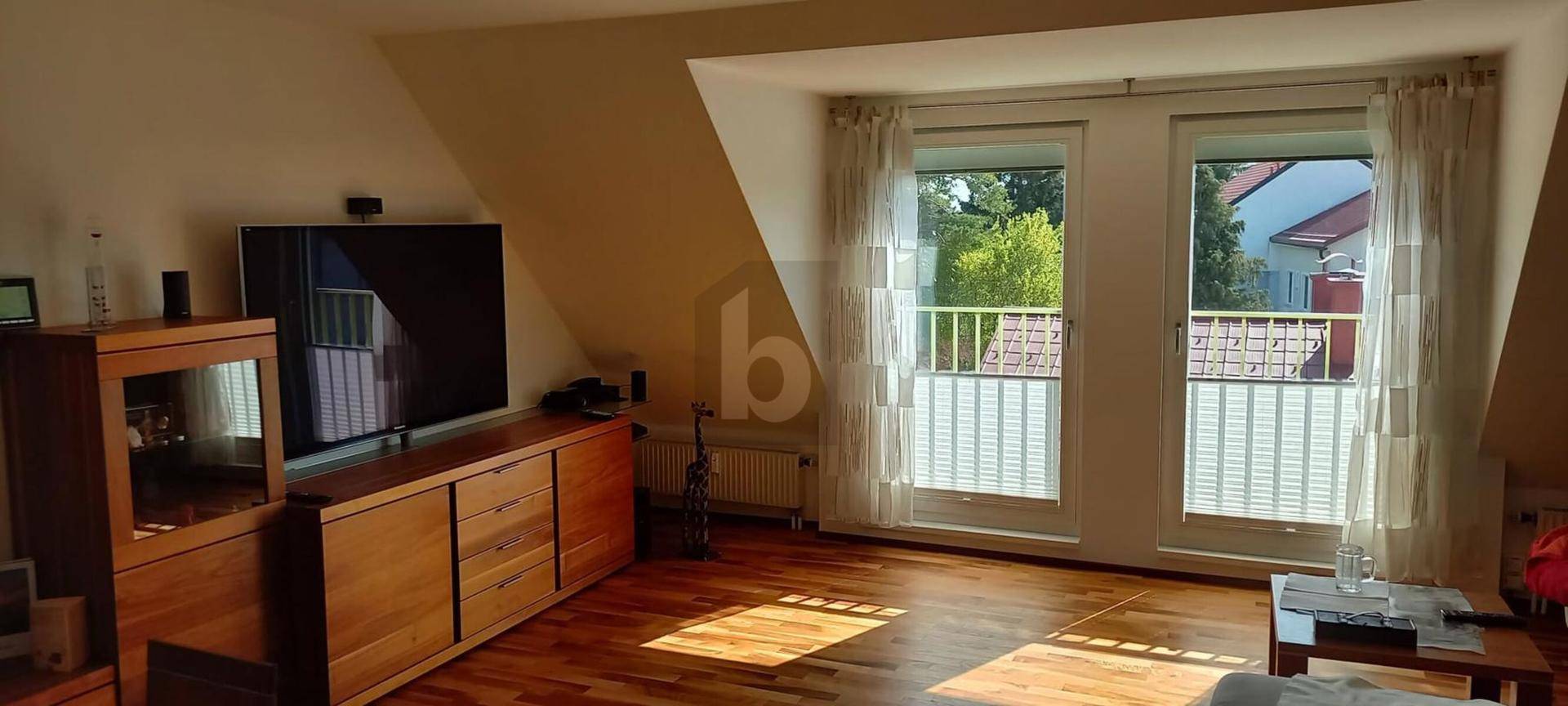 Helles Wohnzimmer im Dachgeschoss mit Holzboden, großem Fernseher und Zugang zu einem französischen Balkon.