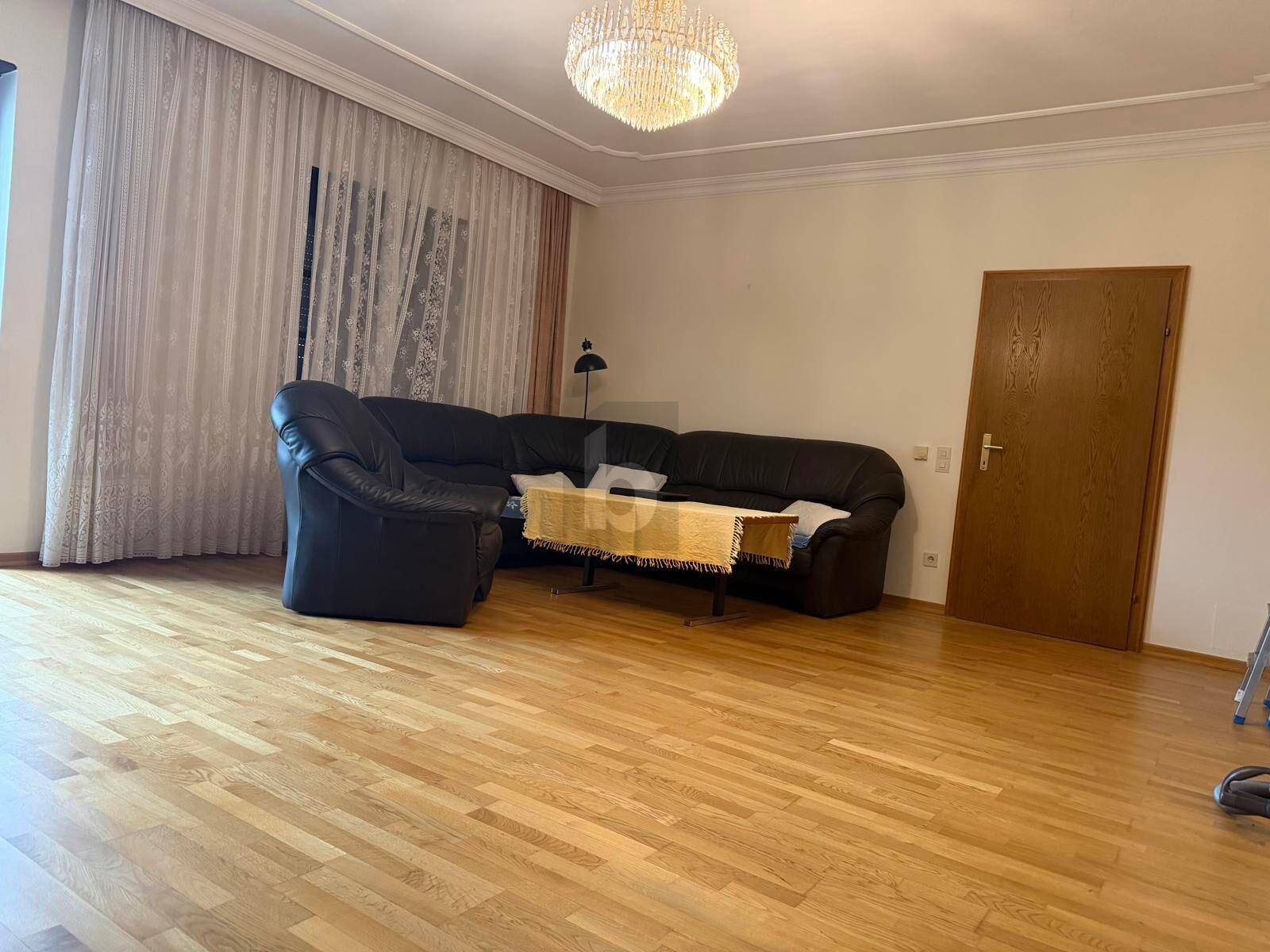 Geräumiges Wohnzimmer mit großem Ecksofa, Parkettboden und einem eleganten Kronleuchter.
