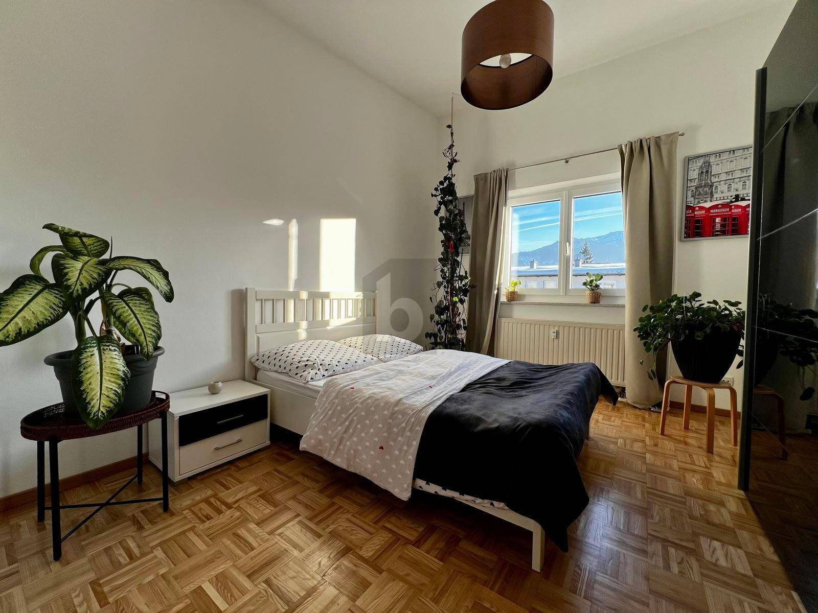 Helles Schlafzimmer mit klassischem Parkettboden, einem Doppelbett und Blick auf die Berge durch das Fenster.