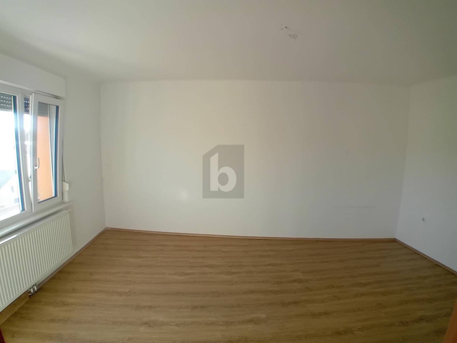 Helles, unmöbliertes Zimmer mit Laminatboden und einem großen Fenster.