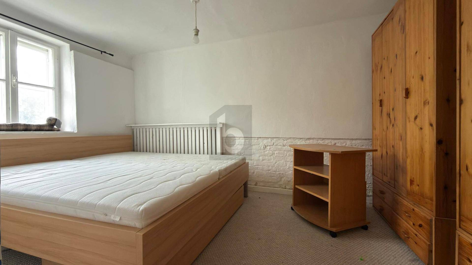Schlafzimmer mit Doppelbett, Holzschrank und Fenster, das auf Renovierung wartet.