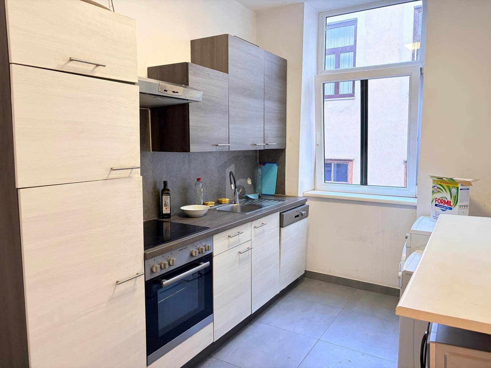 Moderne Küche mit hellen Holzfronten, Einbaugeräten und einem Fenster.