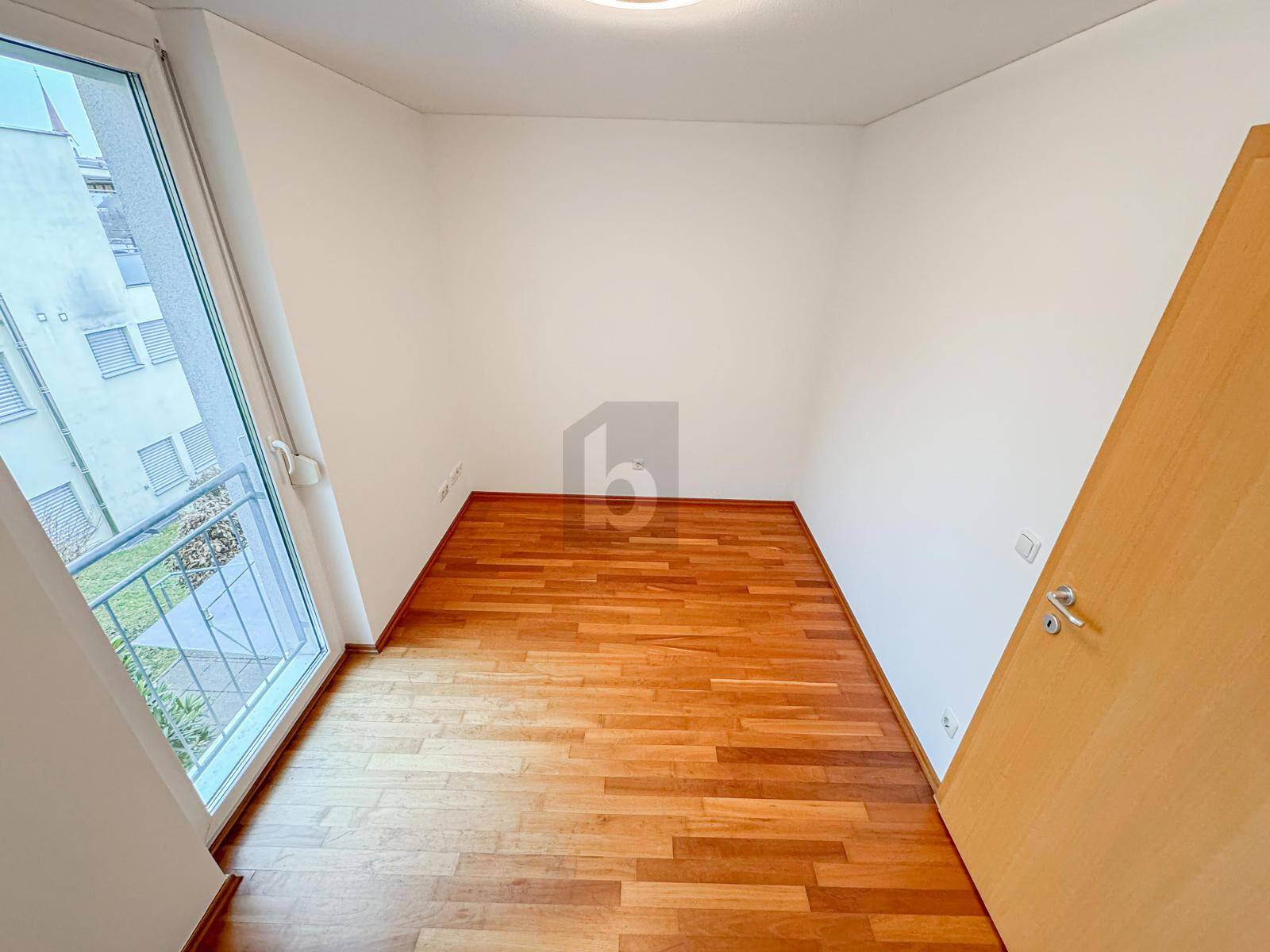 Helles Zimmer mit Parkettboden und großem Fenster, das einen Blick nach draußen bietet.