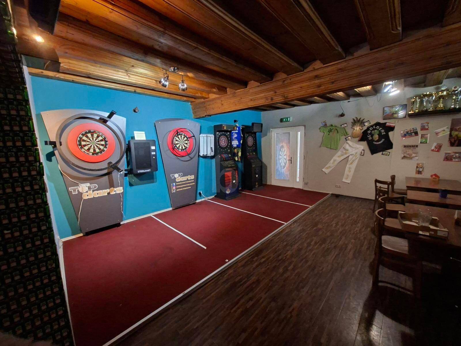 Rustikaler Spielraum mit mehreren Dartscheiben, Holzbalken an der Decke und Teppichboden.