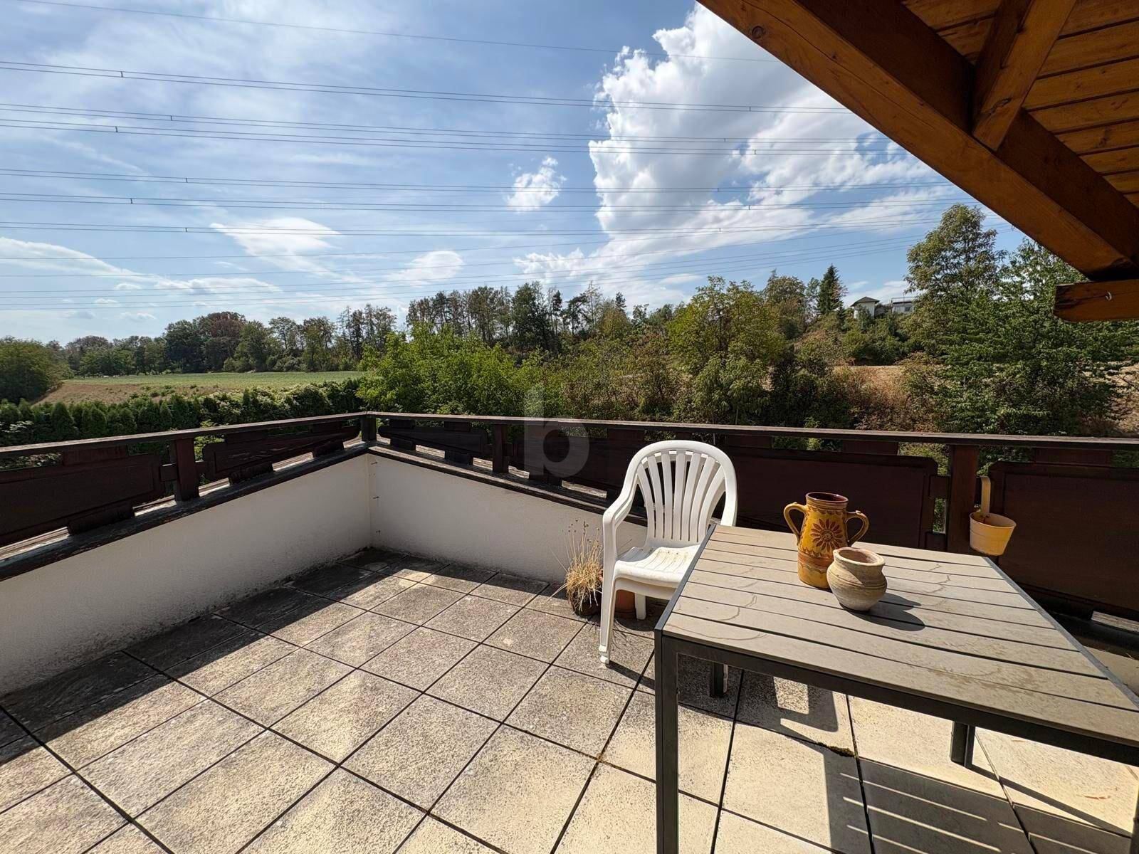 Großer Balkon mit Fliesenboden, Gartenmöbeln und weitem Blick ins Grüne und die Landschaft.