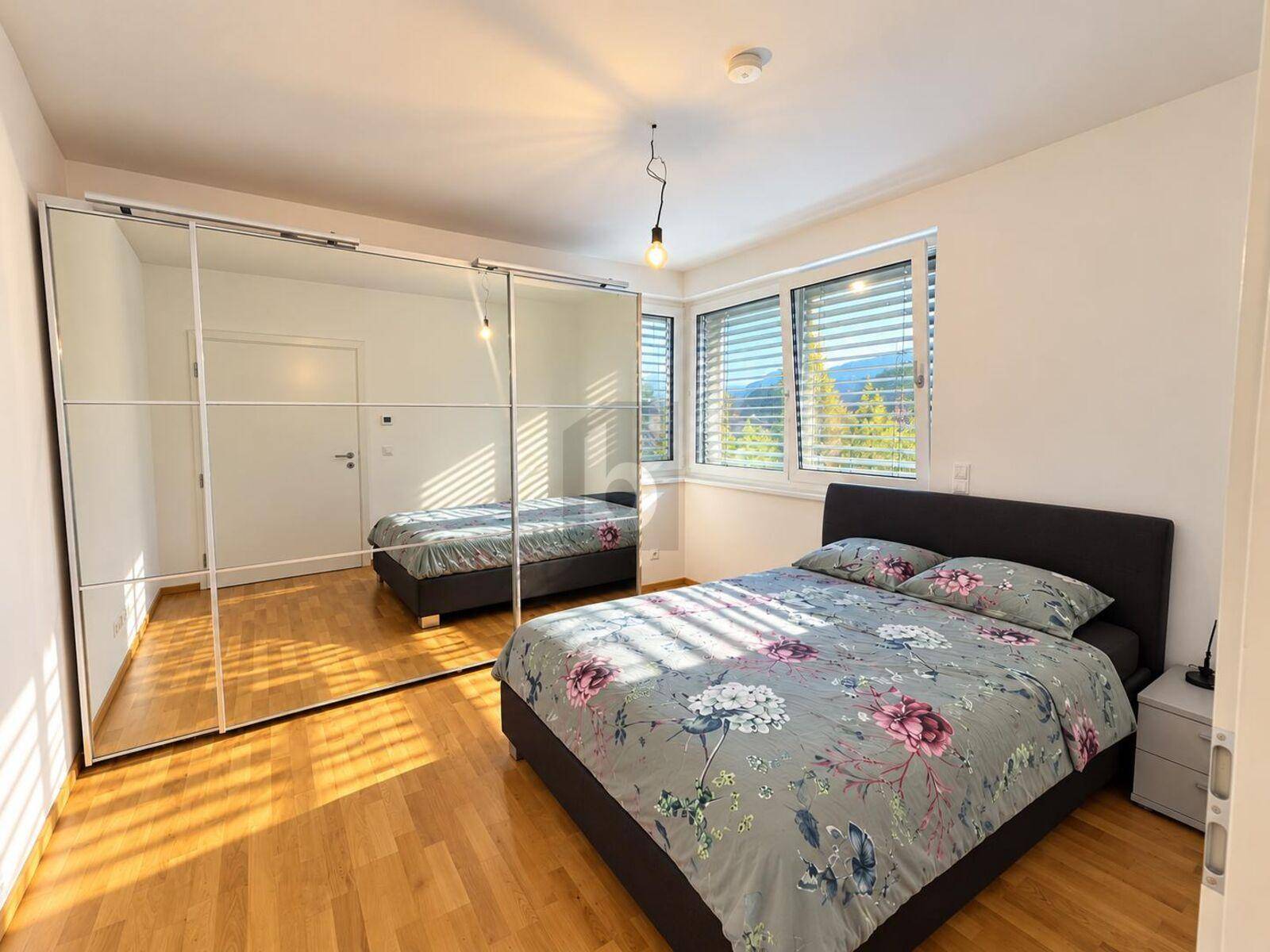 Helles Schlafzimmer mit großem Spiegelschrank, Holzboden und Blick ins Grüne.