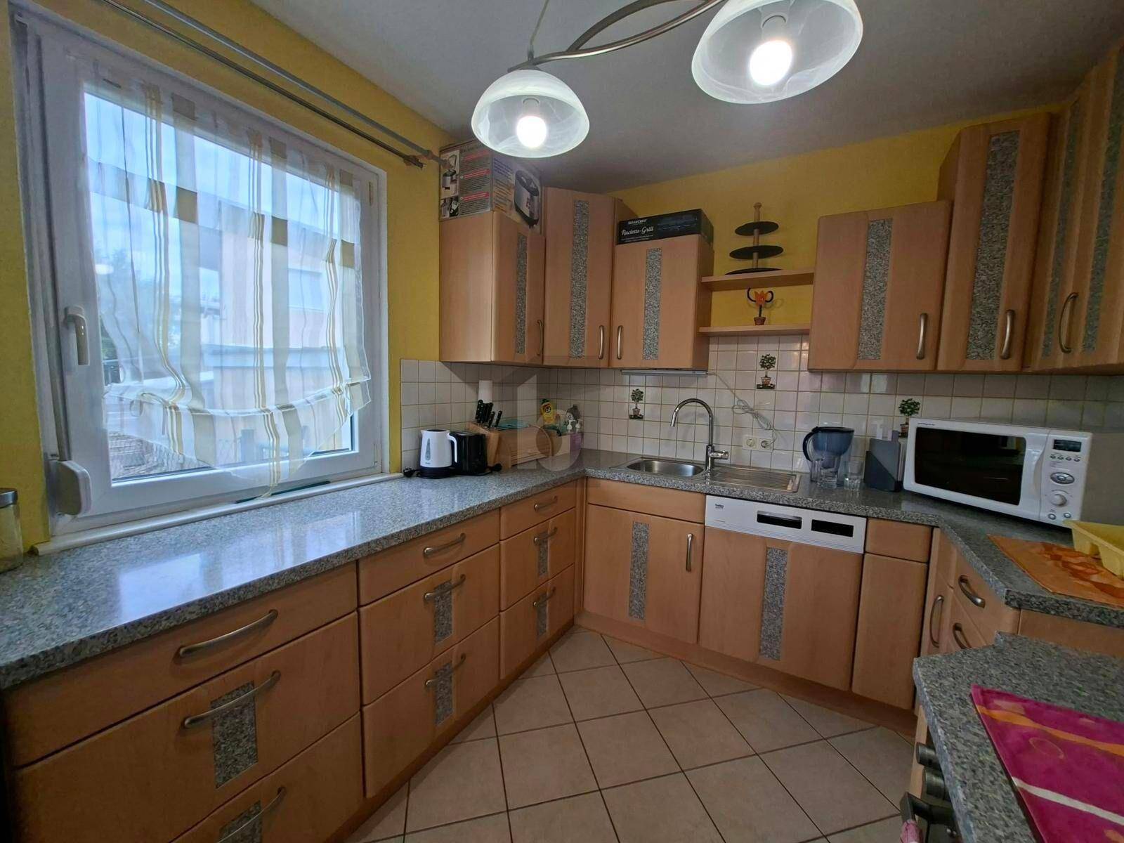 Funktionale Küche mit hellen Holzschränken, Fenster und gefliestem Boden.